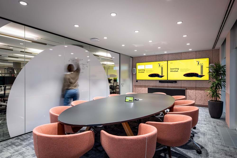 A woman writes on a writable wall in a bright, modern meeting room