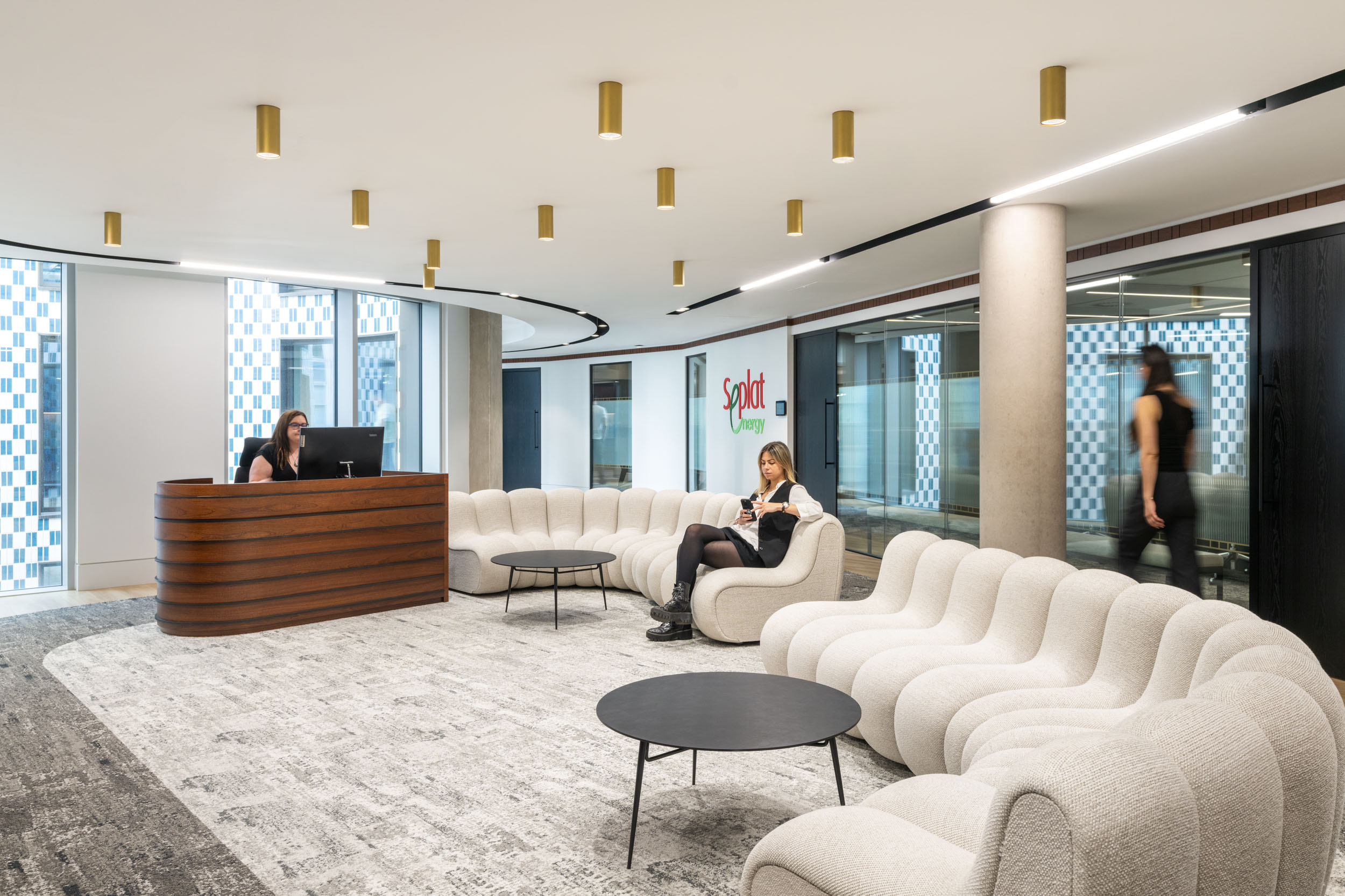 Seplat Energy reception area with bespoke brand signage, large cream sofas, hanging gold lights and employees walking around the space.