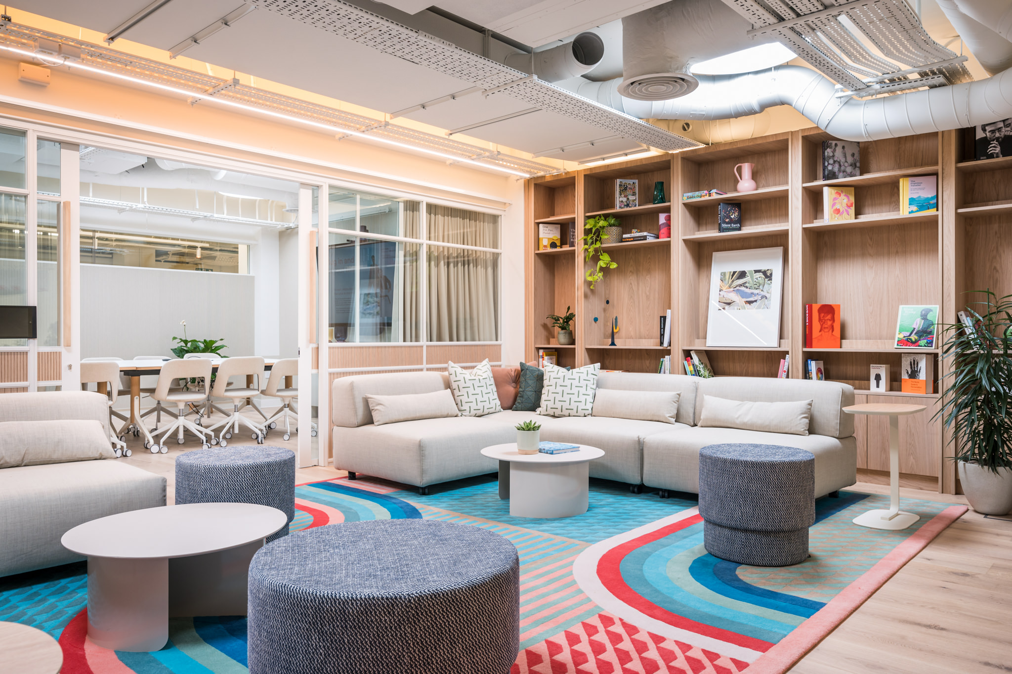 FORA Wells Mews coworking space by Modus showcases a modern, open-plan lounge with comfortable seating, colourful rugs, and a collaborative meeting area in the background.