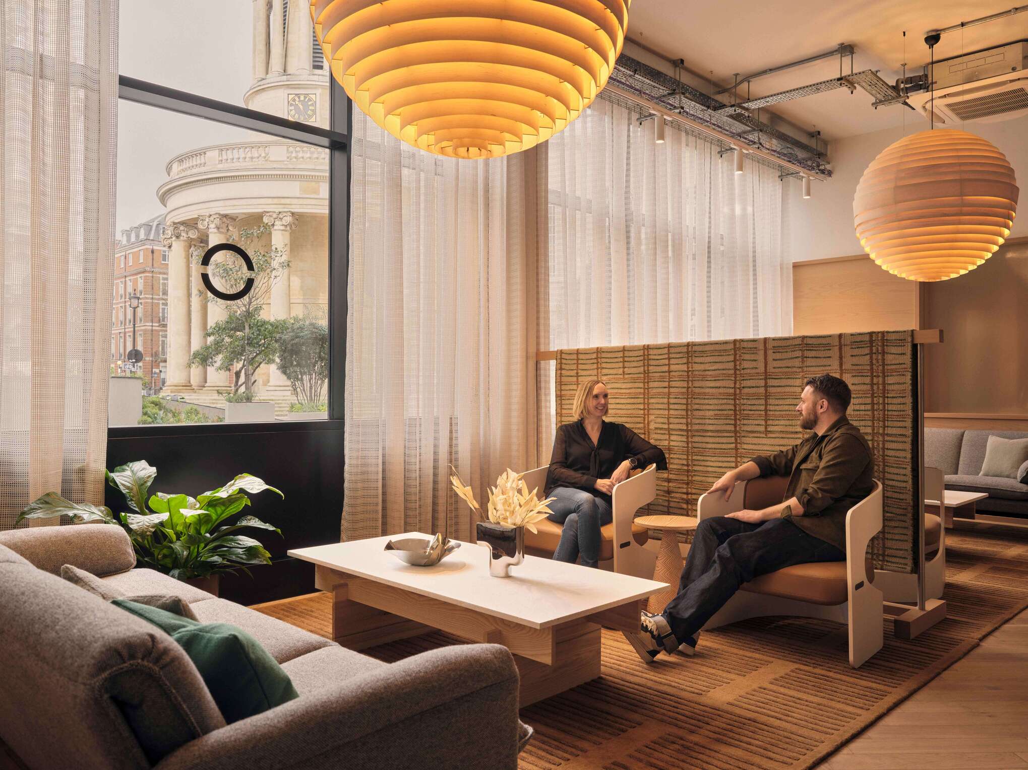 A relaxed meeting space with comfortable seating and large windows that offer views of the surrounding city. The interior uses soft fabrics and wooden accents to create a cozy and inviting environment for discussions and meetings.