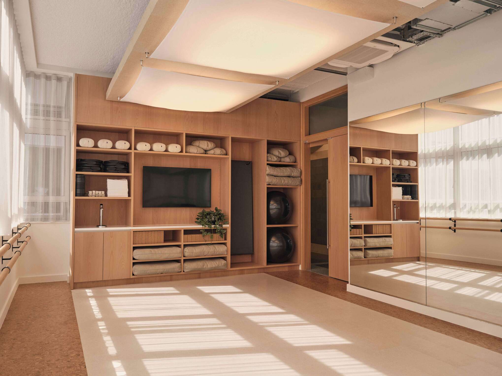 A well-equipped wellness area with a wooden storage system holding towels and gym equipment. The space is designed with ample natural light and a serene atmosphere, providing a calm environment for relaxation and fitness.
