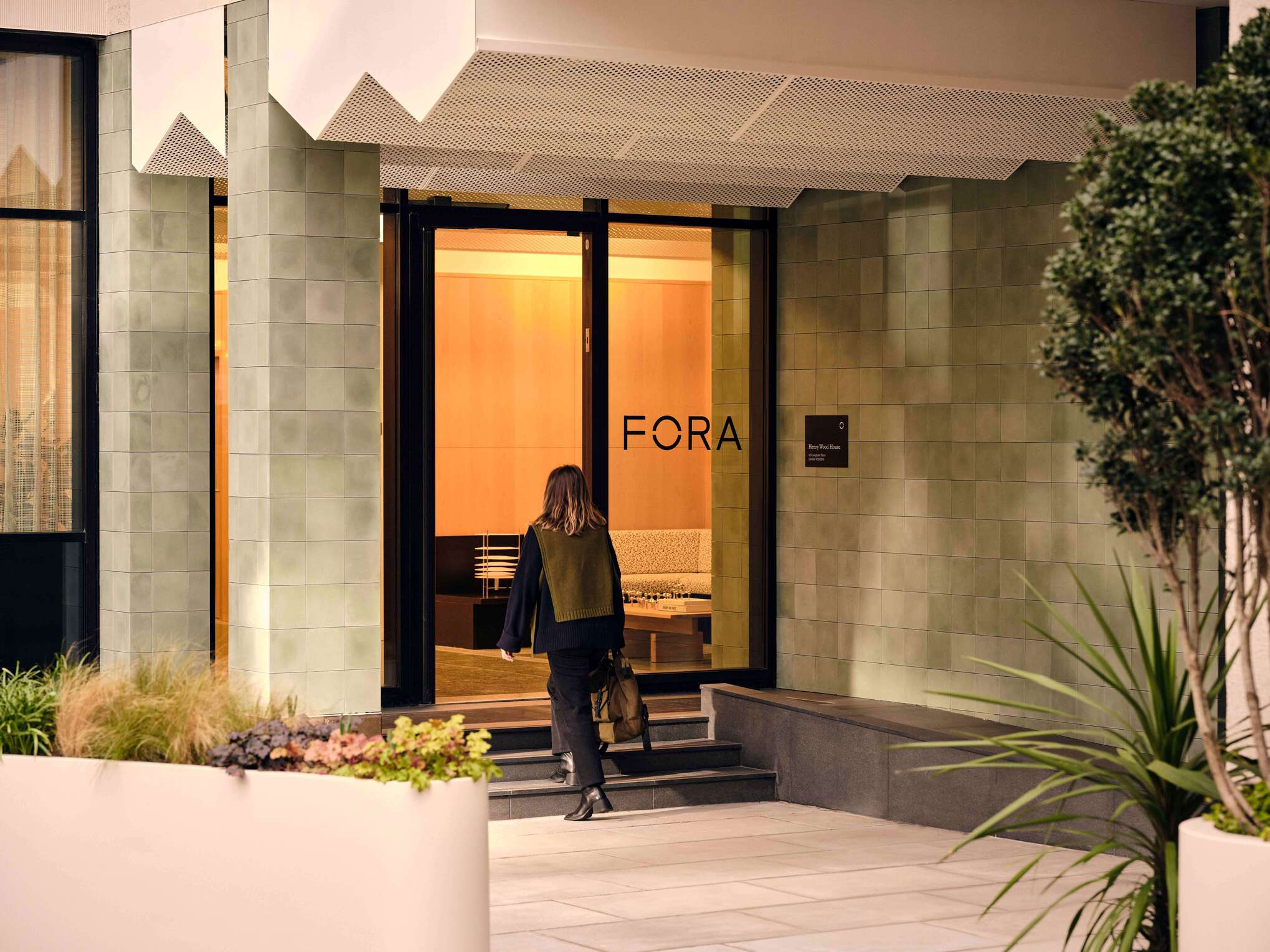 The building's exterior entrance showcasing modern architecture with large, tiled walls and a contemporary design. The entrance has clear signage for Fora and a welcoming pathway flanked by greenery, setting a professional tone for visitors.