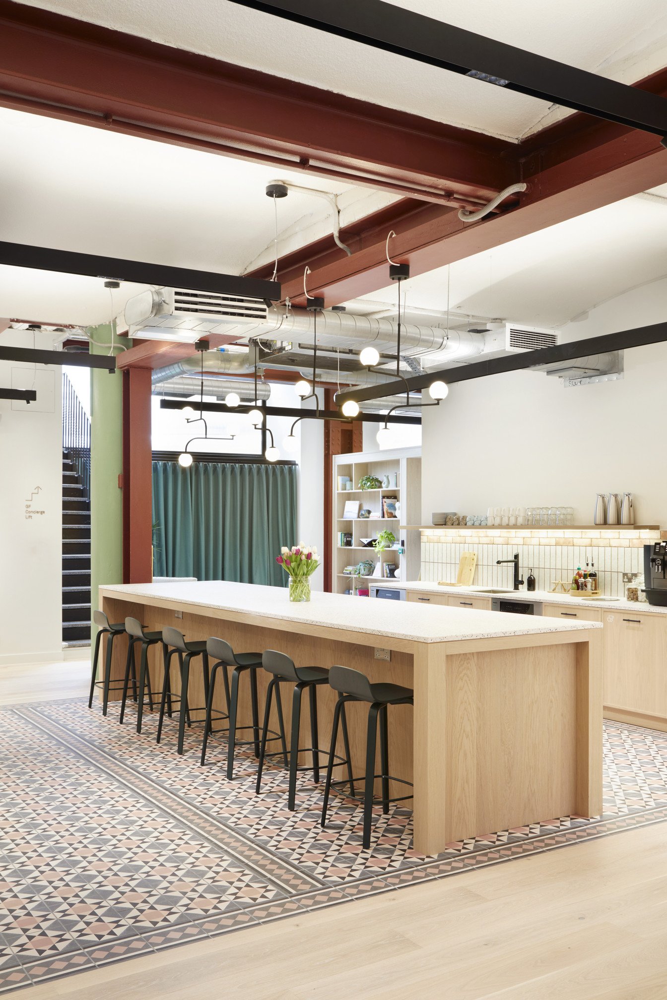 Teapoint at FORA Greencoat Place, featuring a long wooden island with bar stools, patterned flooring, modern pendant lighting, and open shelving.