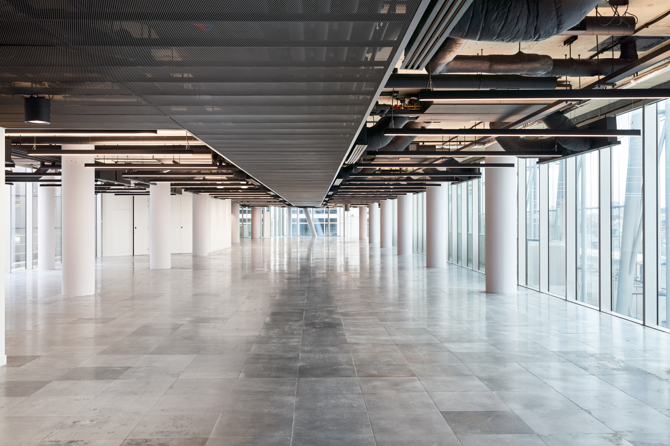 Another view of the expansive office area at 350 Euston Road, designed by Modus, featuring minimalist decor with large windows that flood the space with natural light. The layout includes rows of columns and suspended track lighting, emphasizing the open and flexible workspace.