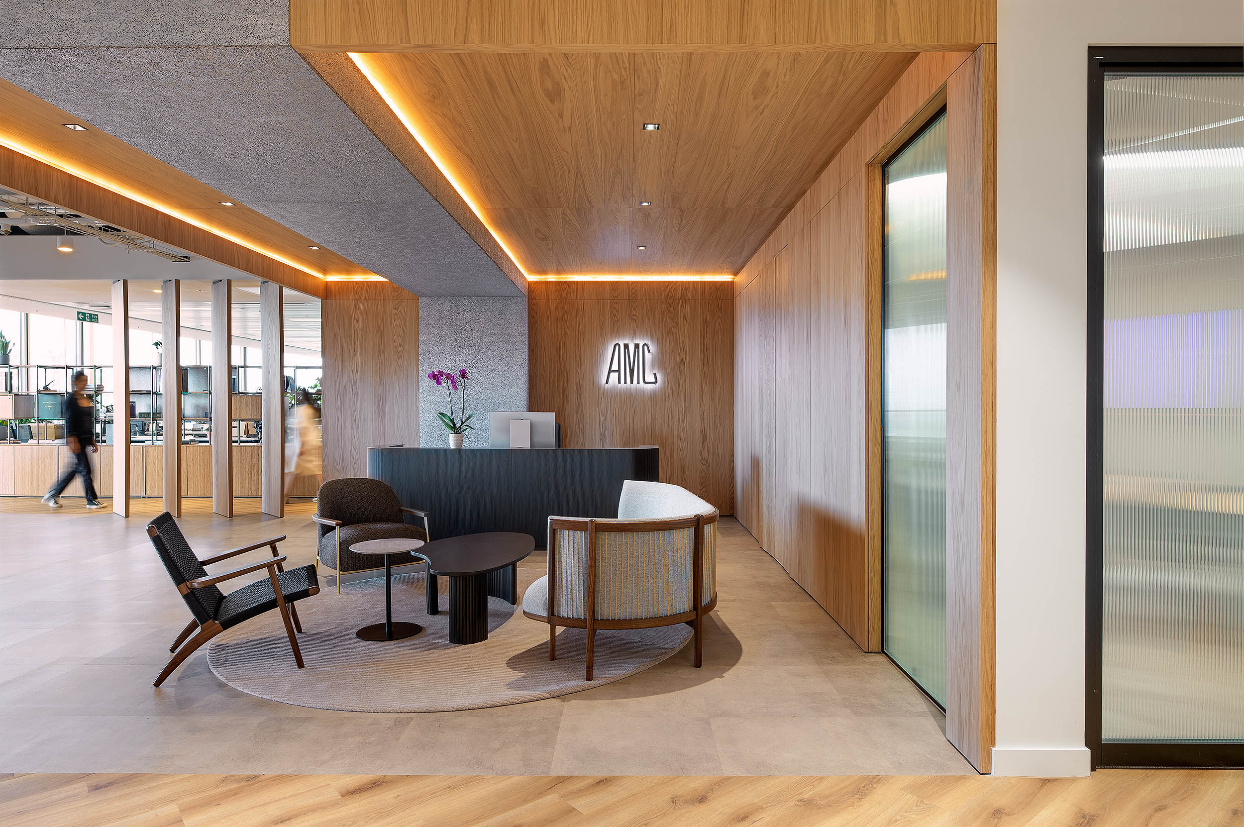 The AMC Group reception features a sleek wooden backdrop, creating a welcoming entrance. The AMC logo is illuminated on the wall.