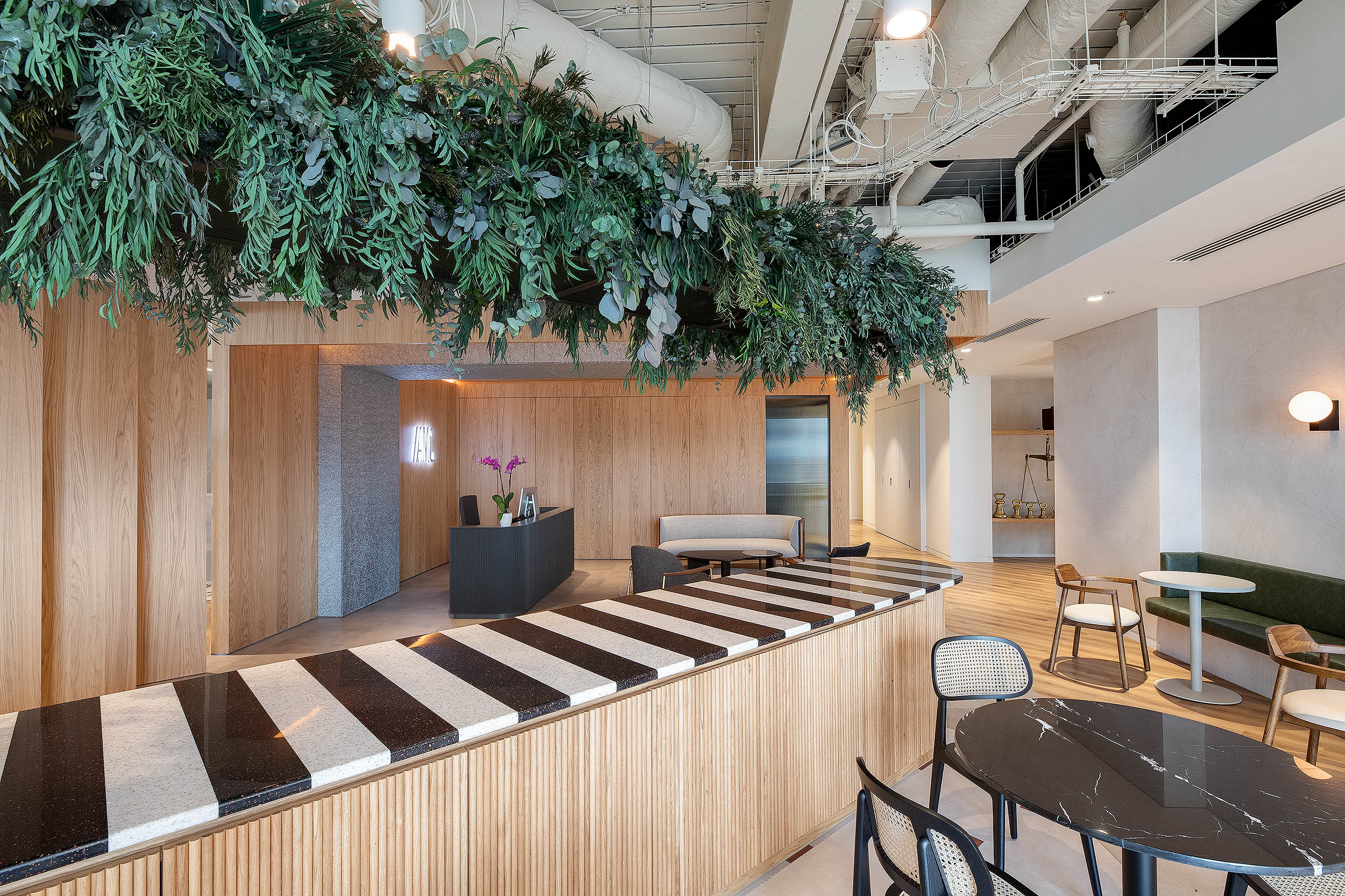 The AMC Group’s office reception and bar area combines a green overhead canopy with modern materials. The bar section features stylish round tables and a contrasting striped countertop.