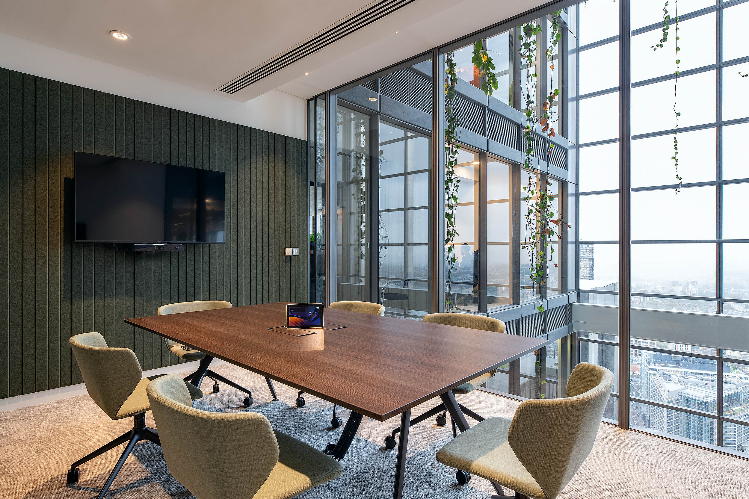 AMC Group meeting room with floor-to-ceiling windows providing panoramic views of the city. This space includes a sleek wooden table and integrated technology with overhanging plants outside the windows.