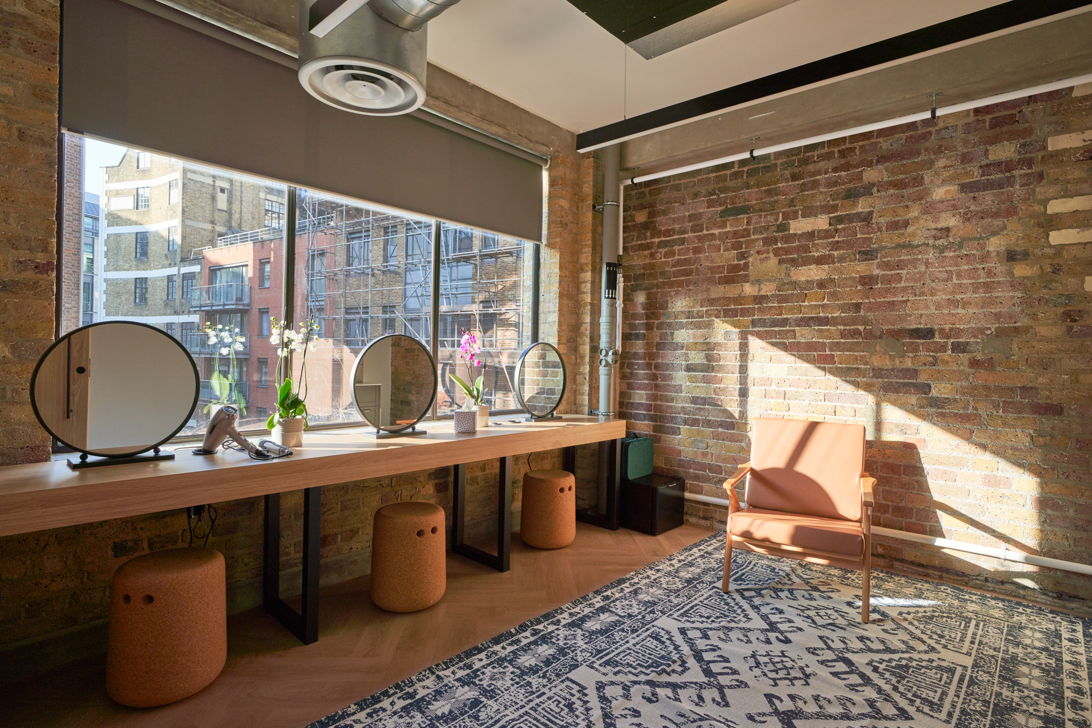 Ayden's unique makeup station against an exposed brick wall, complete with modern circular mirrors and rustic wooden detailing. The natural light and earthy tones create a warm, inviting space for personal grooming.