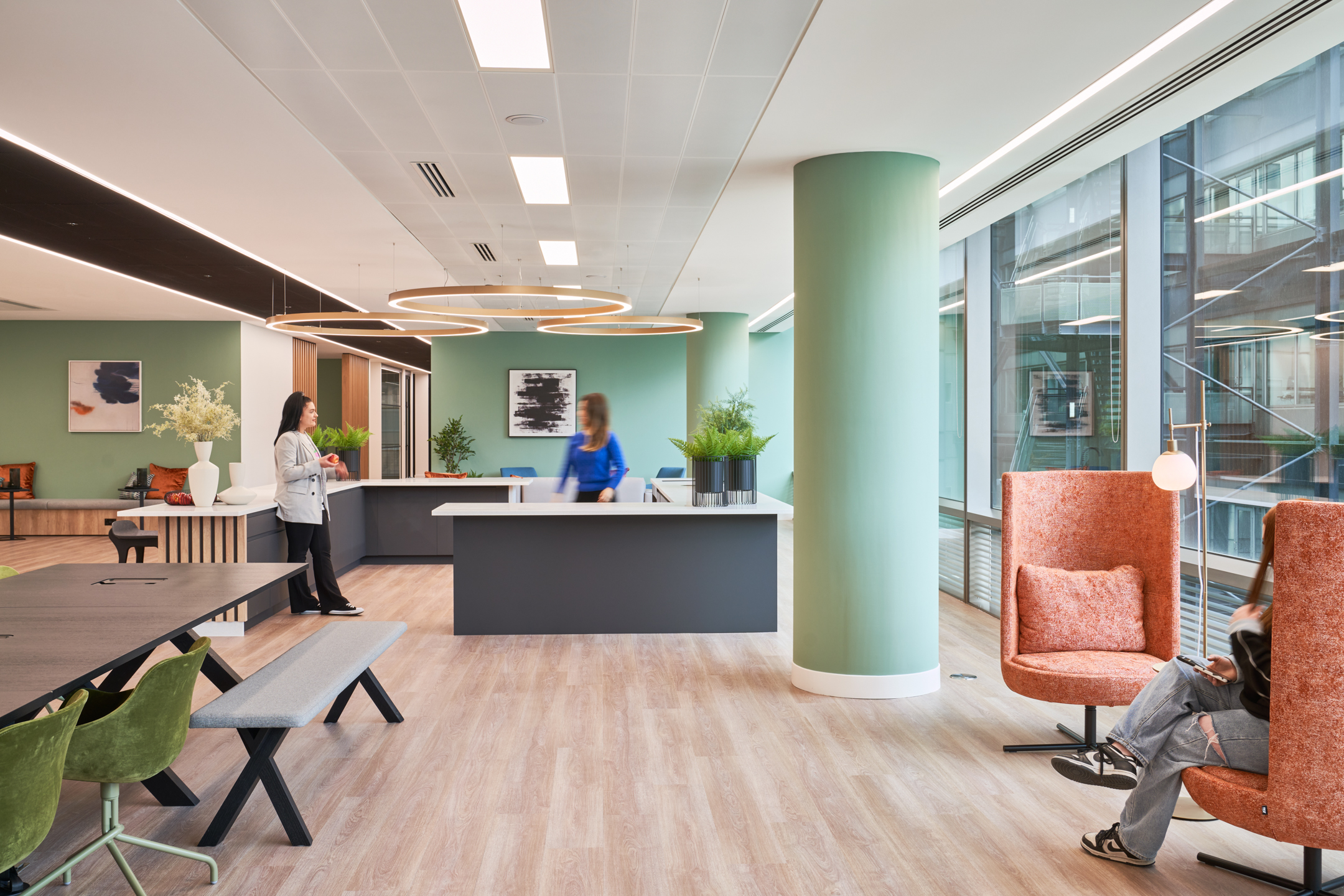 A versatile office space at British Lands 10 Exchange Square, designed by Modus Workspace, with green pillars and modern furnishings. People are seen engaging in casual conversations and work activities.