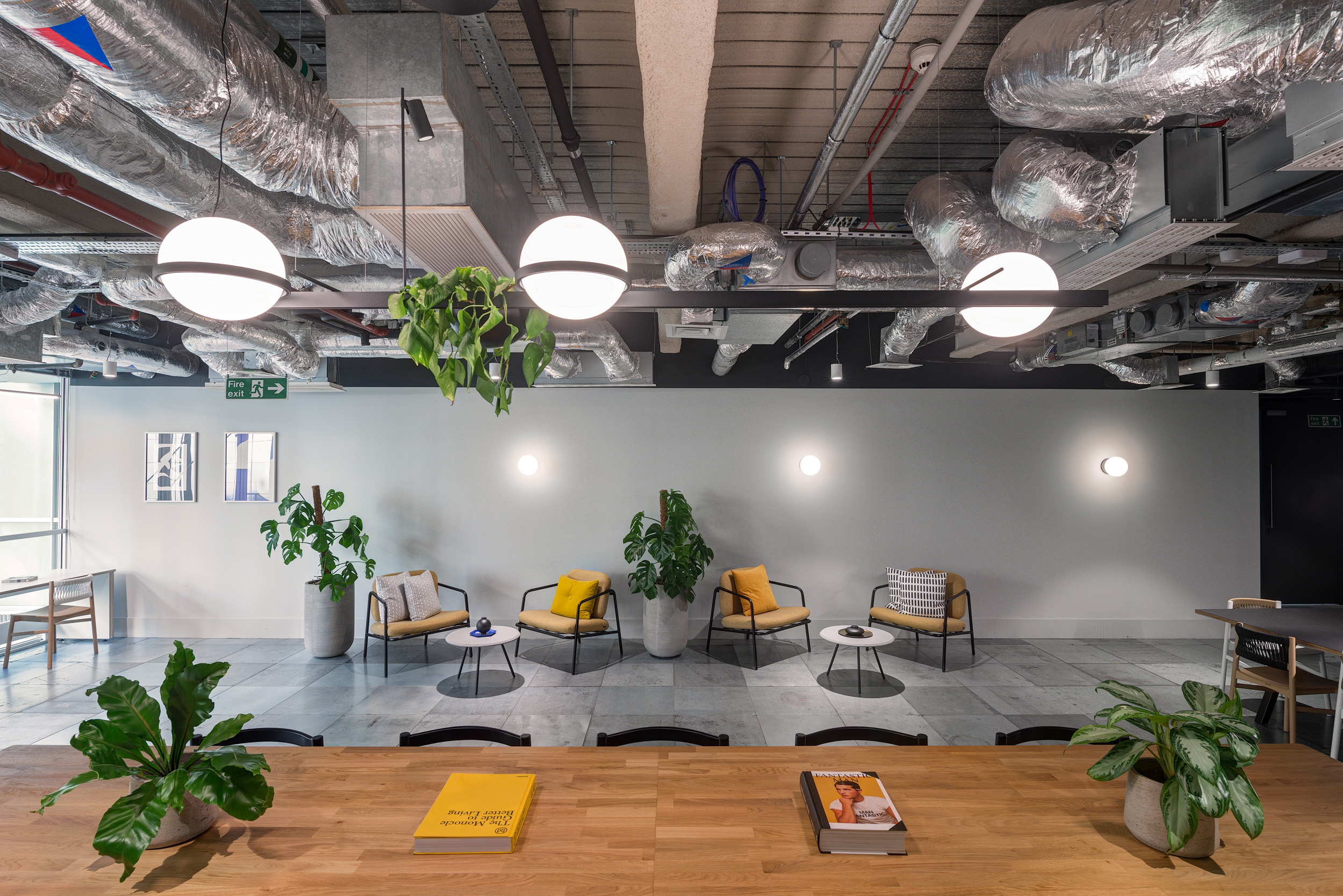 A modern communal area in the British Land office at 3 Finsbury Avenue, designed by Modus Workspace. The space is characterized by a long central table surrounded by chairs, with stylish overhead lighting and a backdrop of functional kitchen facilities.