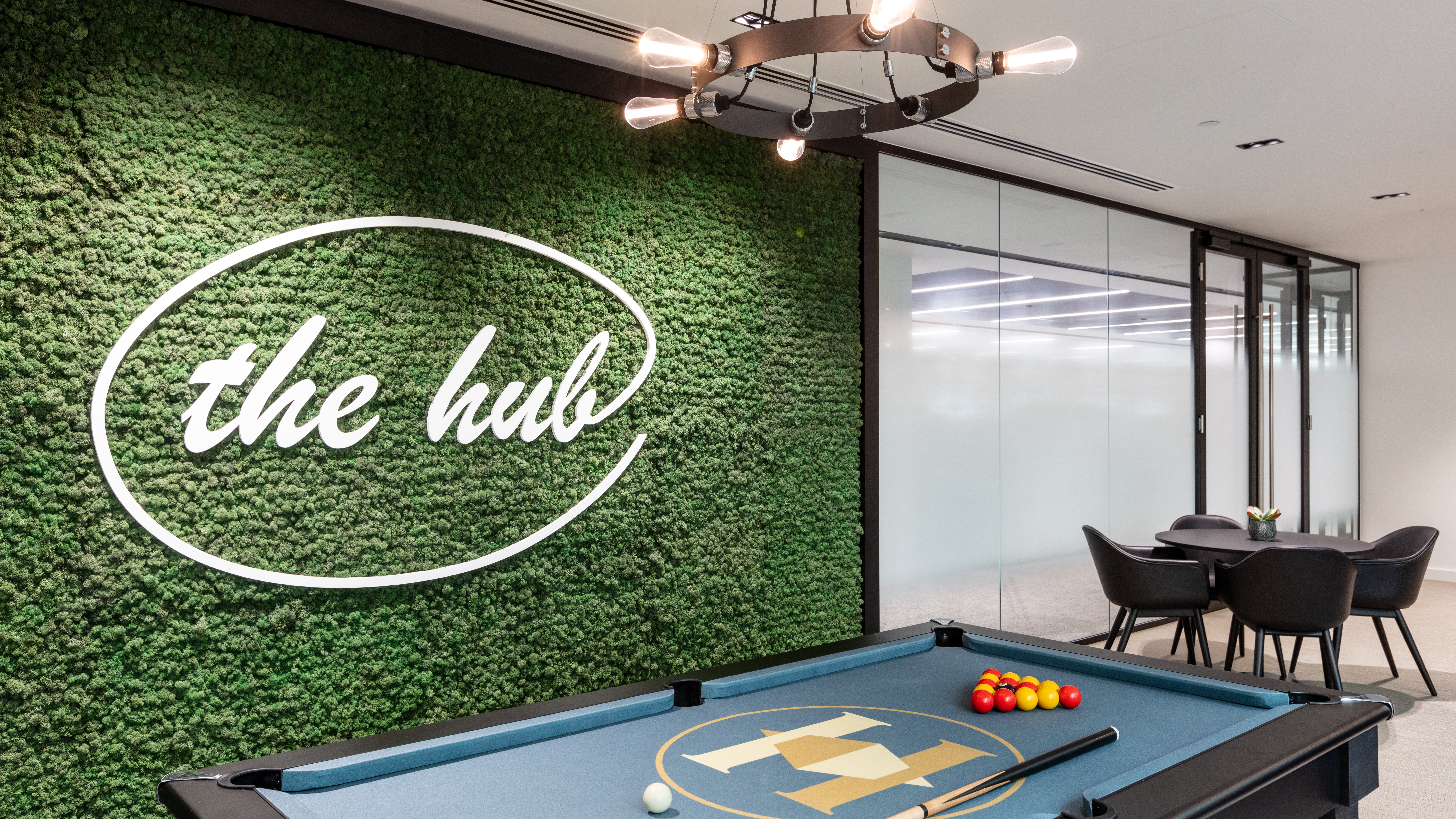 The Hub at Houlihan Lokey features a pool table against a striking green moss wall, designed by Modus Workspace to encourage creativity and relaxation. This area serves as a social space for employees to unwind.