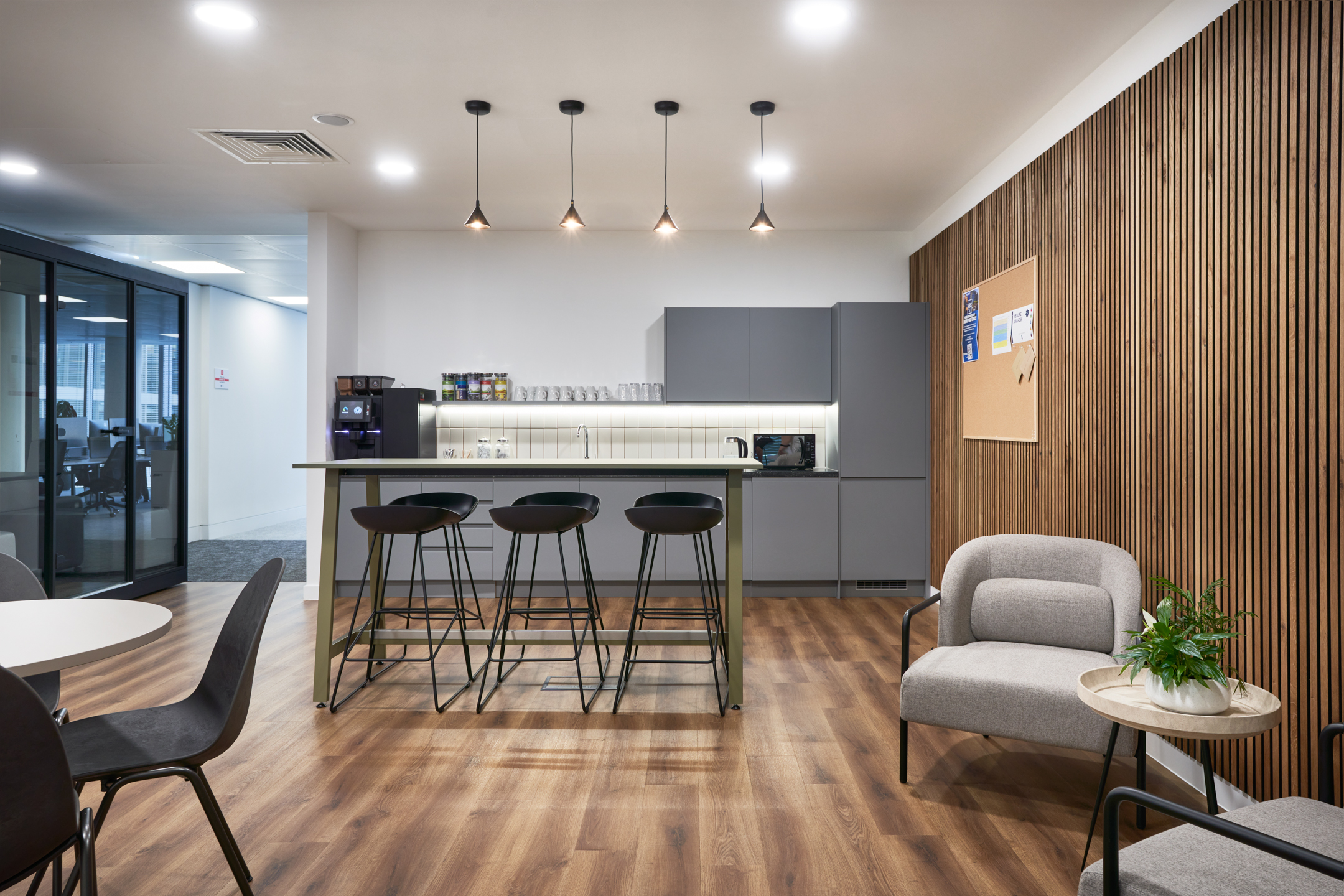 The teapoint area within LGC's 100 Victoria Street office, designed by Modus Workspace, features warm wooden flooring, a high counter with seating, and stylish pendant lighting, creating a welcoming environment for breaks.