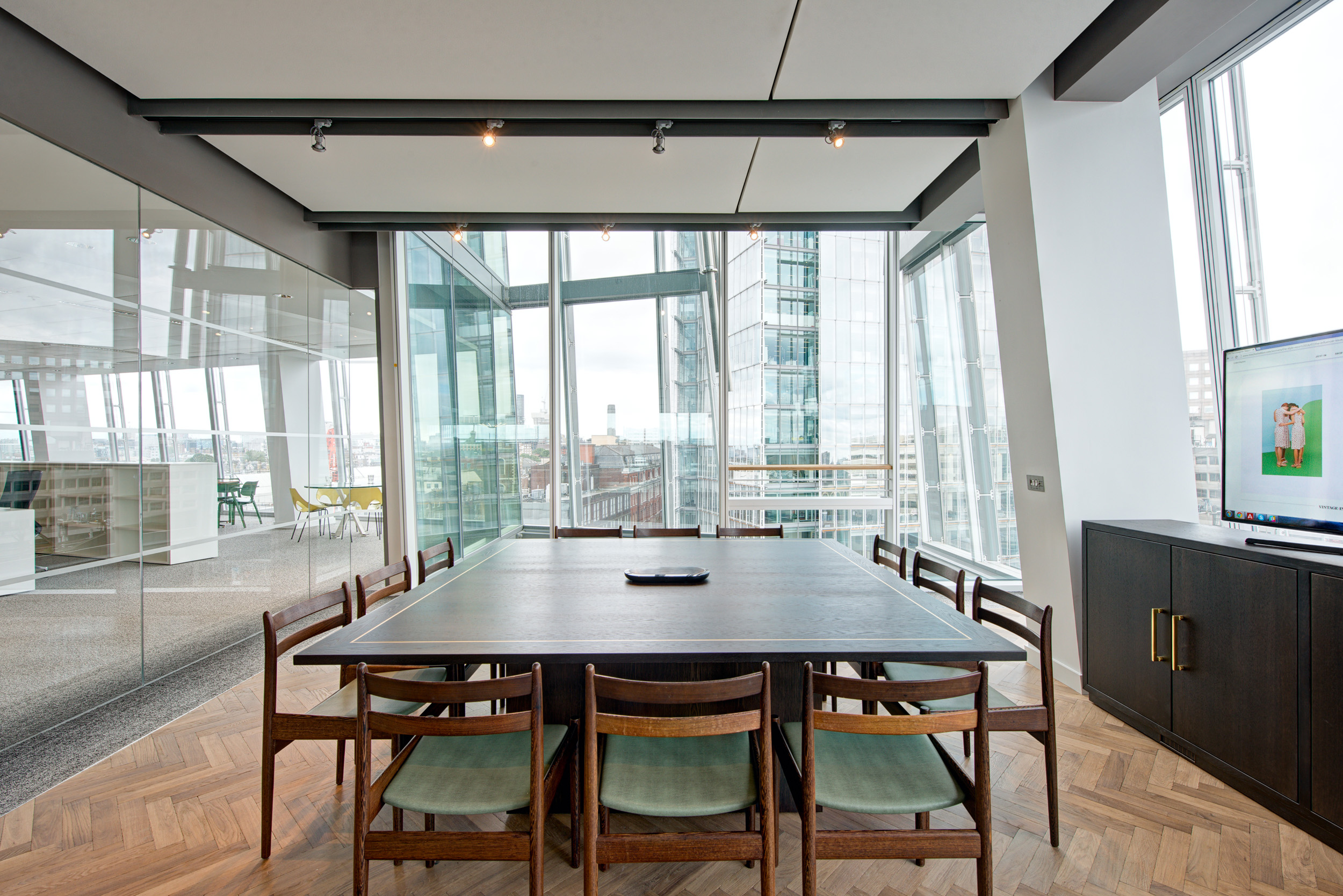 Glass-fronted meeting room and focus booths at Matches Fashion, designed by Modus Workspace, provide a sleek and private space for discussions. A blurred figure walks past, highlighting the dynamic environment within the office.