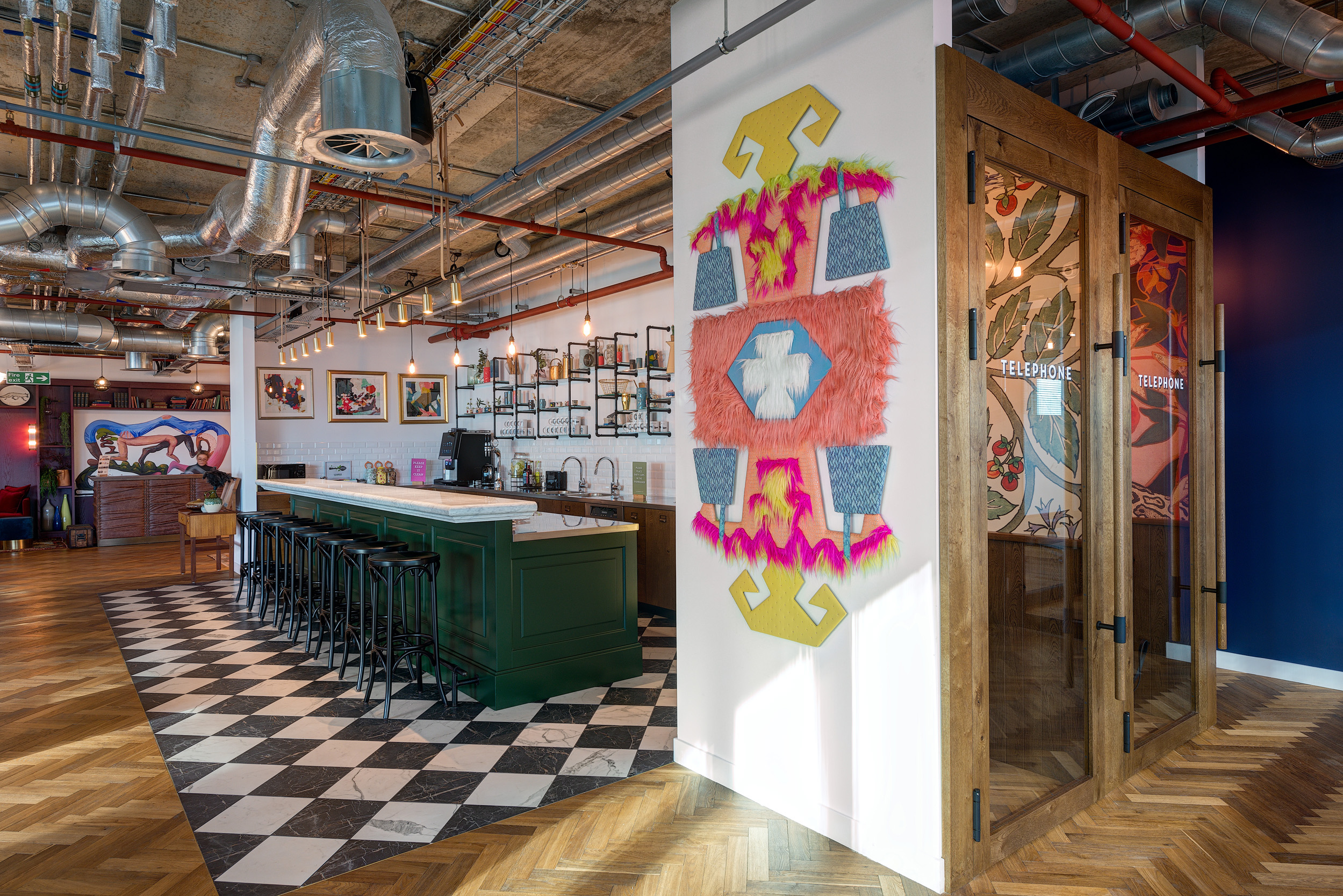 A view of the distinctive bar area with checkered flooring and bold wall art next to telephone booths at Mindspace 144 Whitechapel, designed by Modus Workspace.