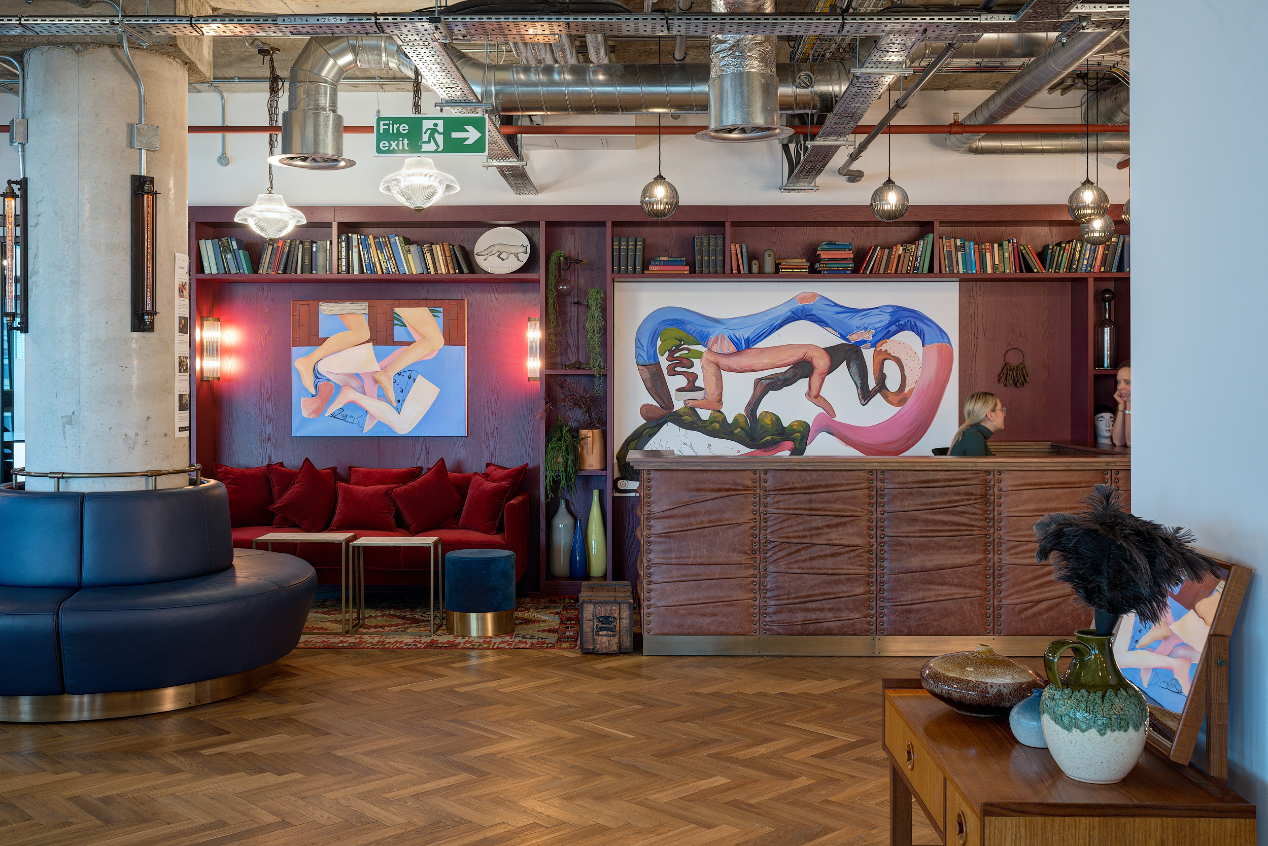 The reception area at Mindspace Aldgate with a red velvet sofa, a large painting, wooden bookshelves and biophilic plants.