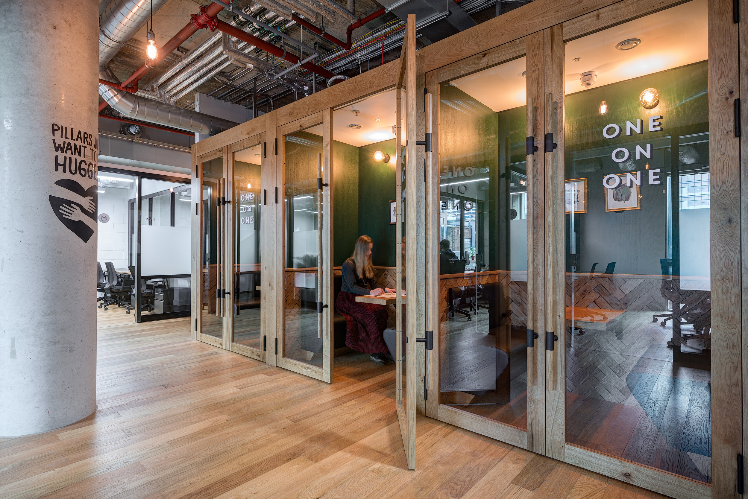 A row of glass-walled private meeting pods featuring natural wood and green accents at Mindspace 144 Whitechapel, designed by Modus Workspace.
