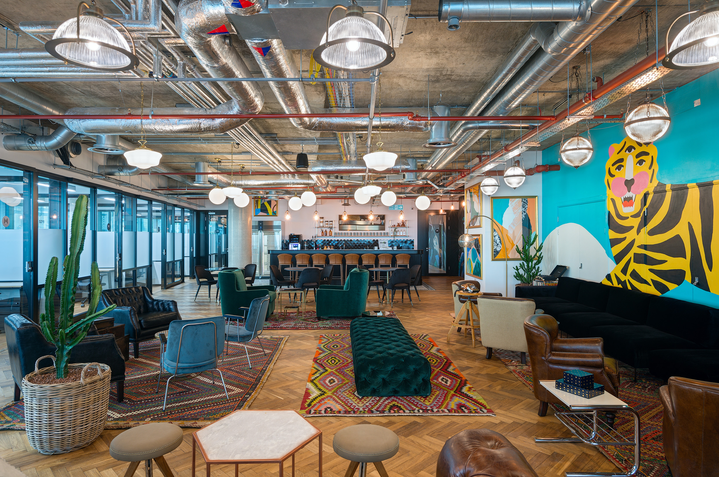 A spacious lounge with eclectic seating, bold artwork, and an open bar area at Mindspace 144 Whitechapel, designed by Modus Workspace.