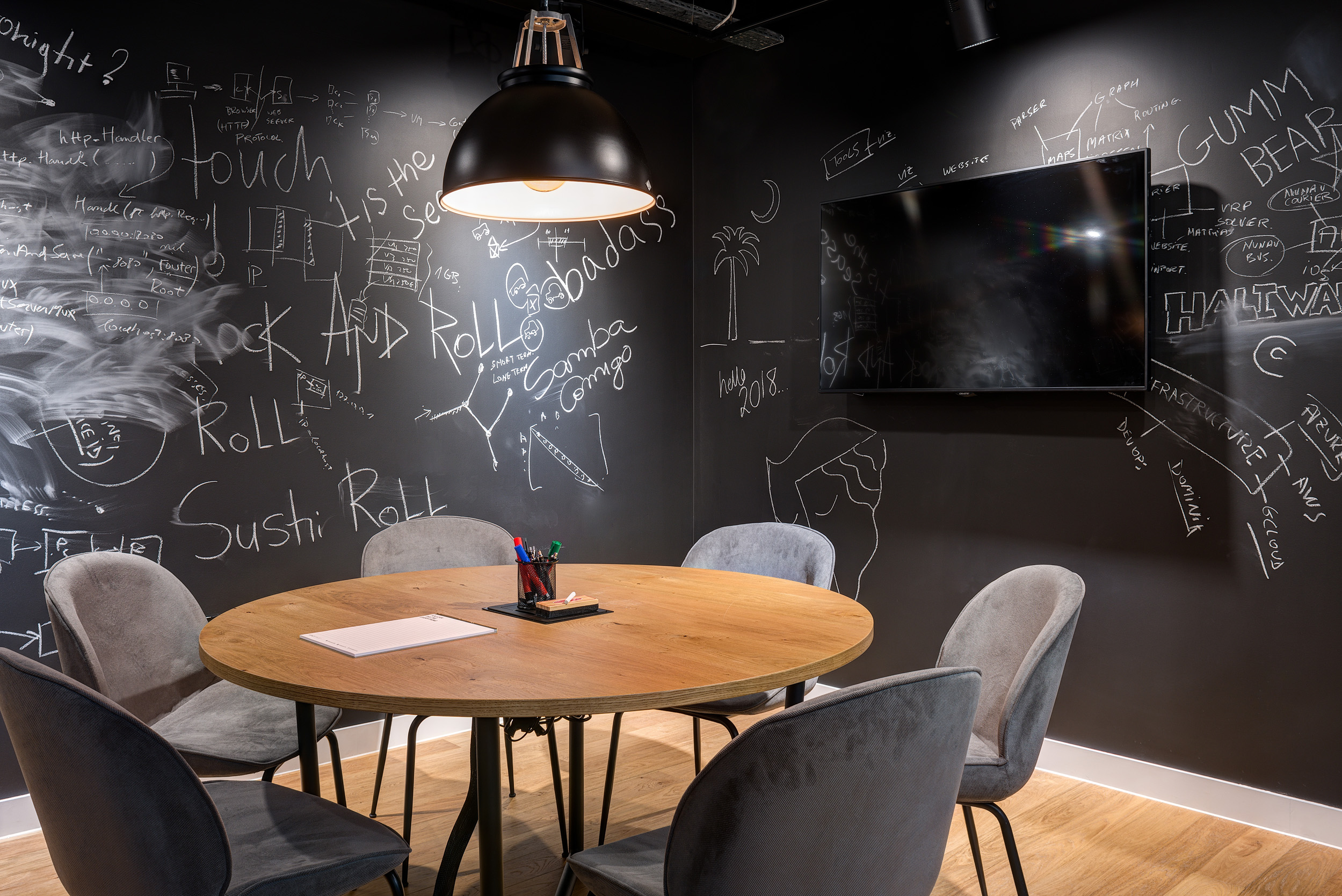 A black meeting room with white chalkboard designs and a wooden table at Mindspace, designed by Modus Workspace.