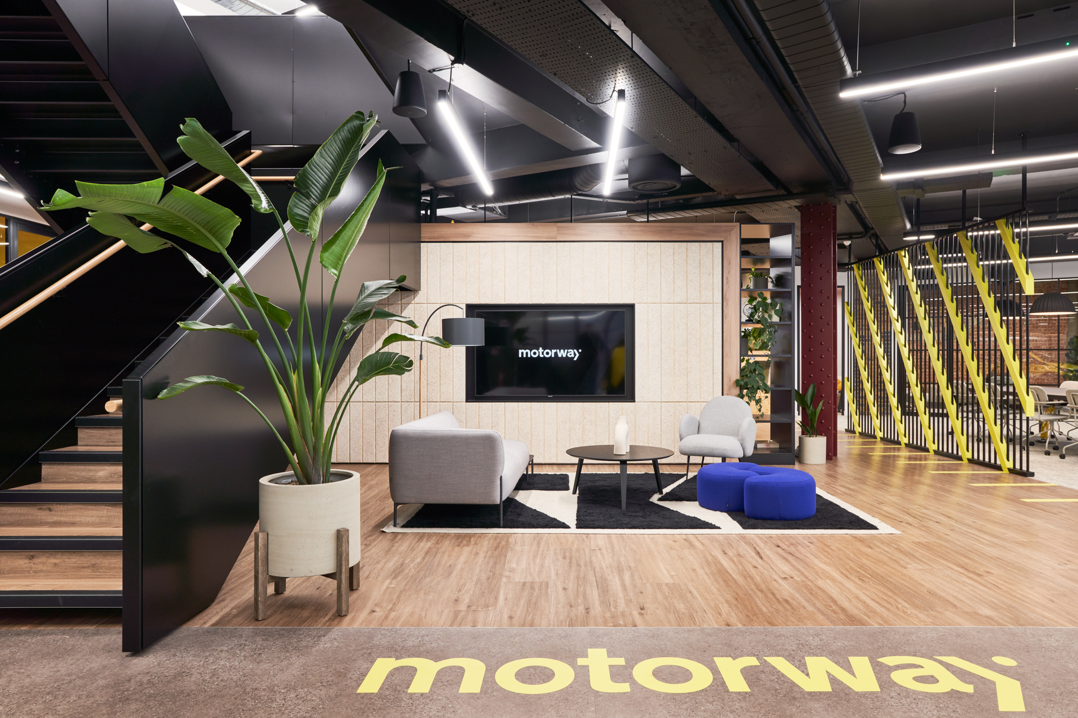 Motorway yellow branding with a large plants displayed on the black metal staircase.