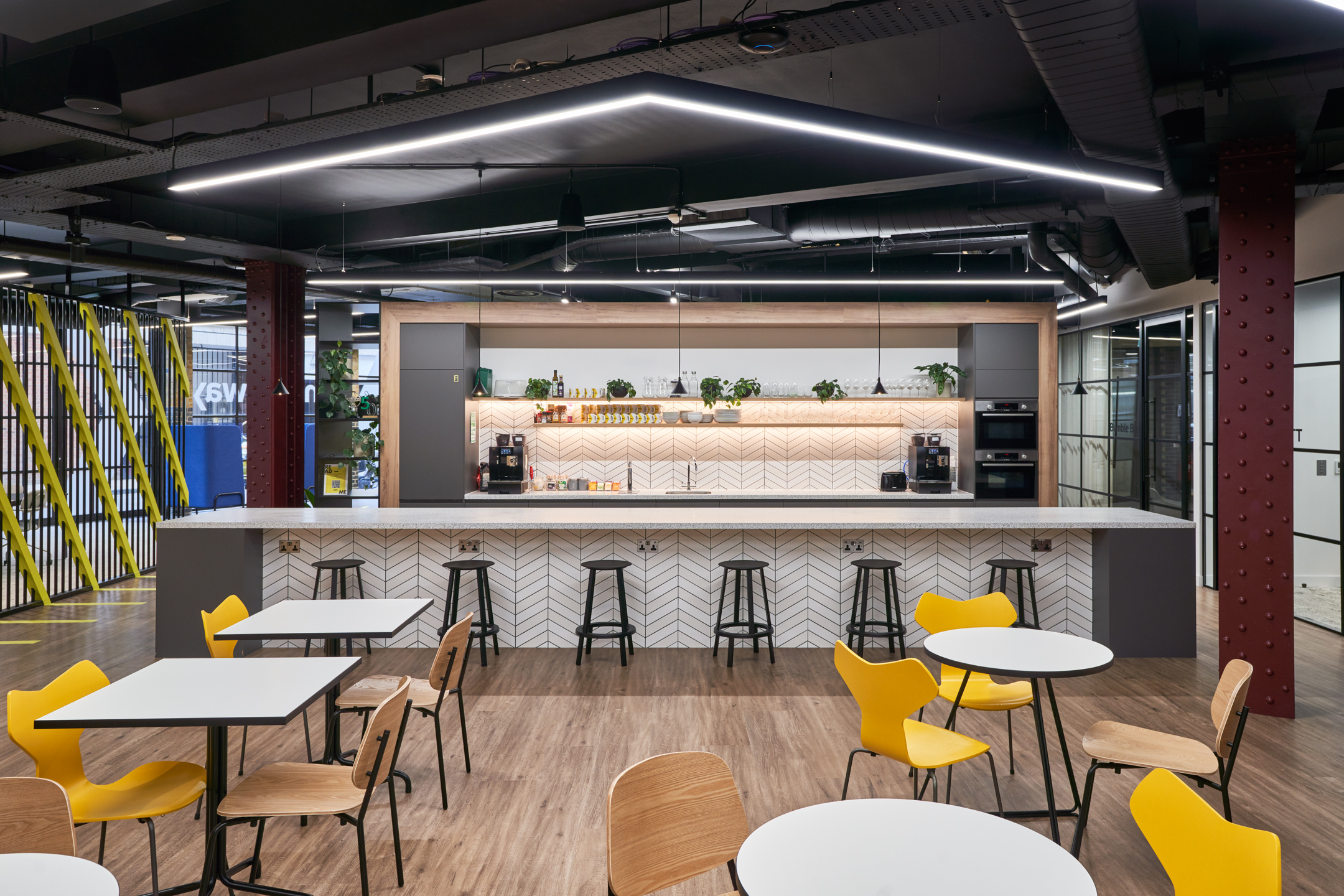 Motorway teapoint with matching island and kitchen splashback tiles, high stools and hanging arrow shaped lights.