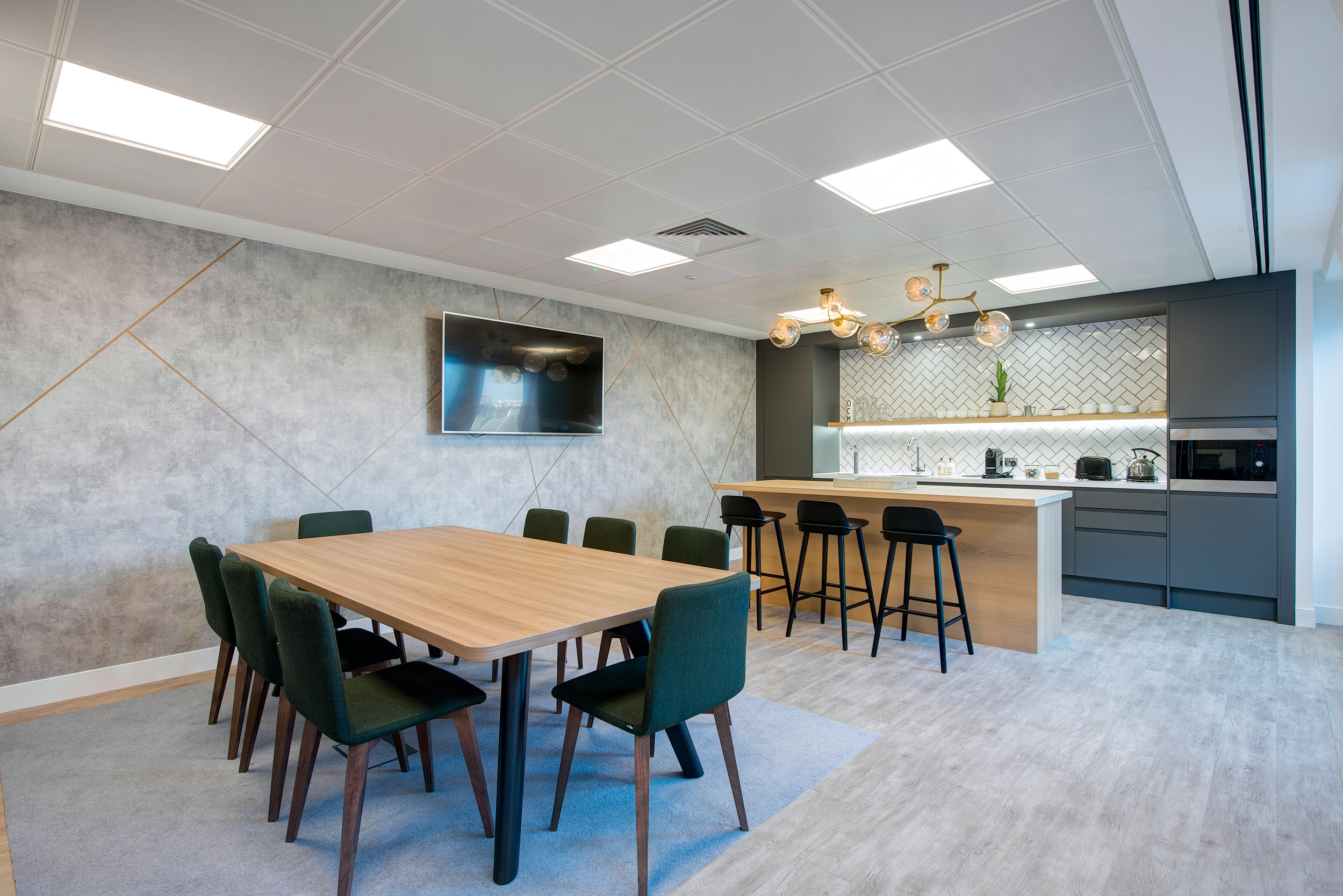 A contemporary teapoint and dining space within Otus Capital Management, designed by Modus Workspace, showcasing a minimalist design with a central dining table, comfortable seating, and a modern kitchenette, perfect for casual meetings and breaks.