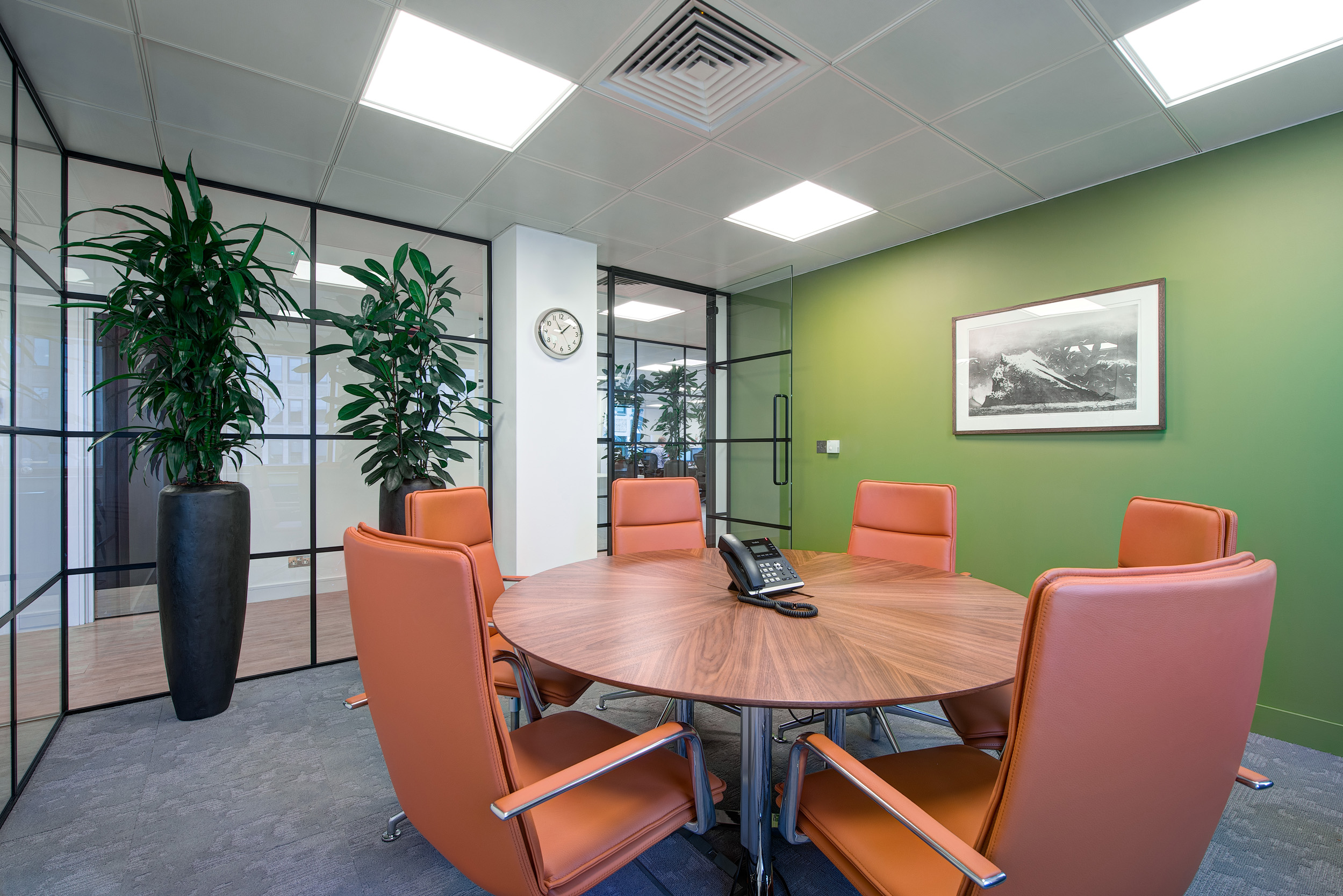 A private meeting room at Otus Capital Management, designed by Modus Workspace, with a round wooden table and leather chairs, complemented by greenery and a large, framed artwork, creating a conducive environment for discussions.