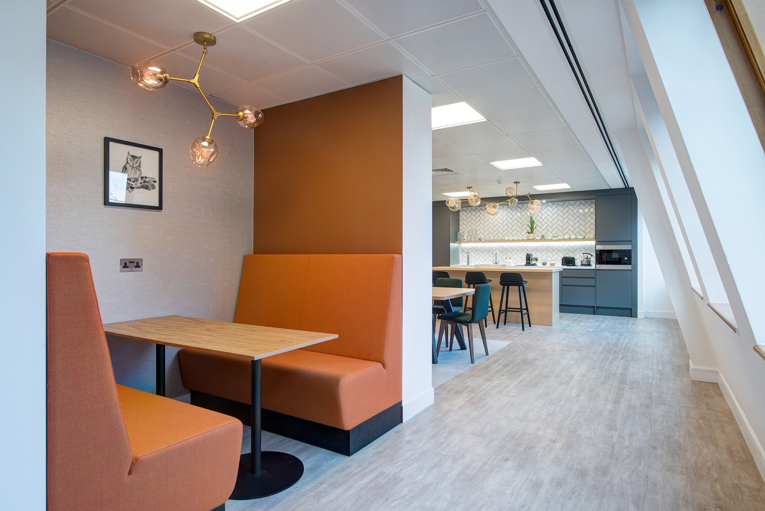 A cosy breakout area within Otus Capital Management, designed by Modus Workspace, featuring plush seating, a modern lighting fixture, and a view of the open teapoint area, encouraging relaxation and informal conversations