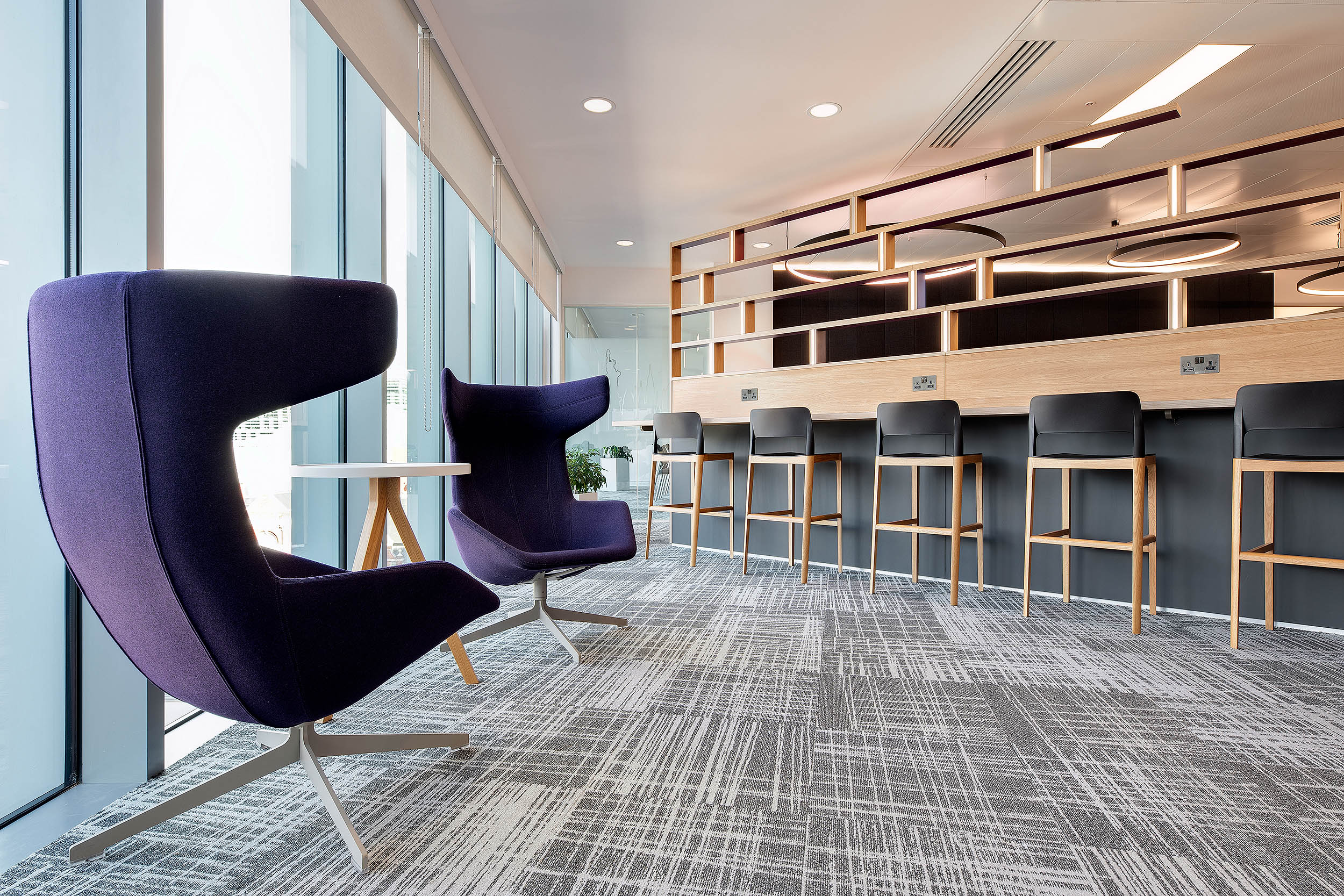 A breakout and flexible working area at RICS with purple chairs, high stools along a bar-style table, large windows, and a mix of seating options.