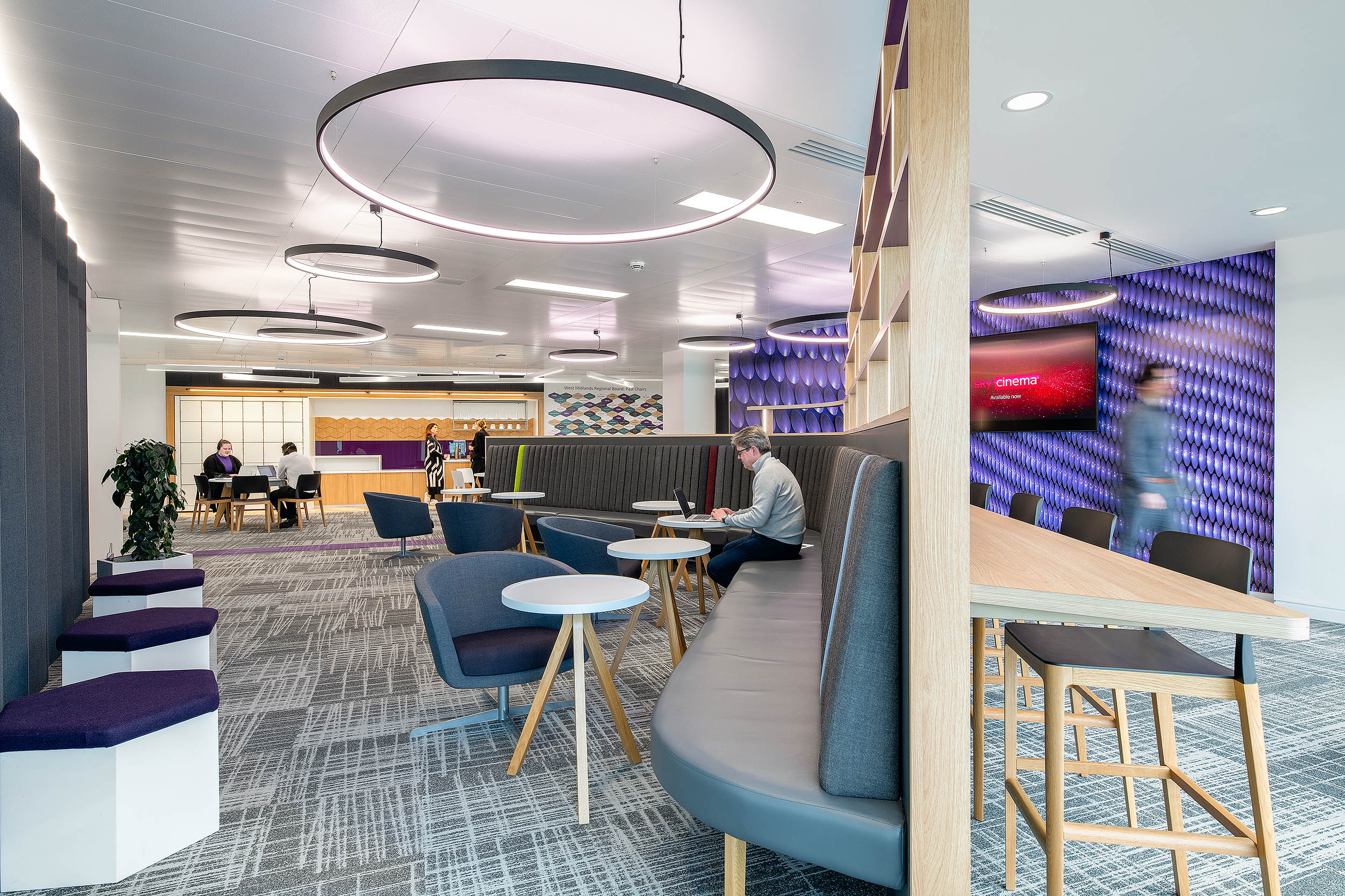 Open breakout area at RICS with curved booth seating, round tables, grey chairs, and a textured purple backdrop.
