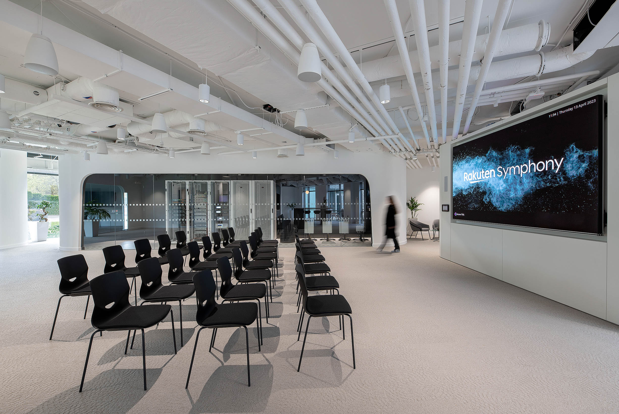 Rakuten symphony screening room with black seats, white open space, and an employing waling through the space