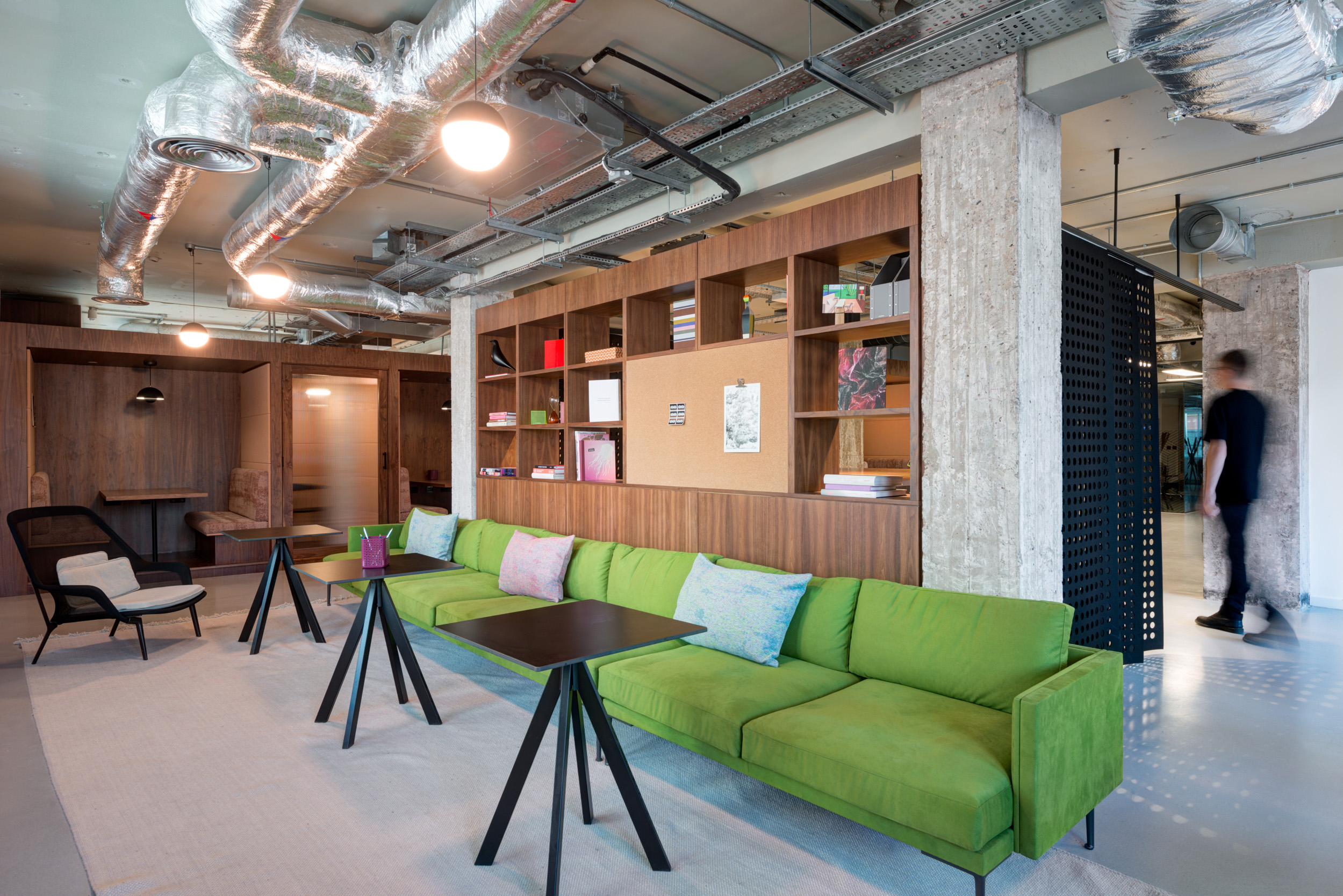 Green sofa with wooden shelving and exposed ceiling pipes in a breakout area at Spaces Peter House.