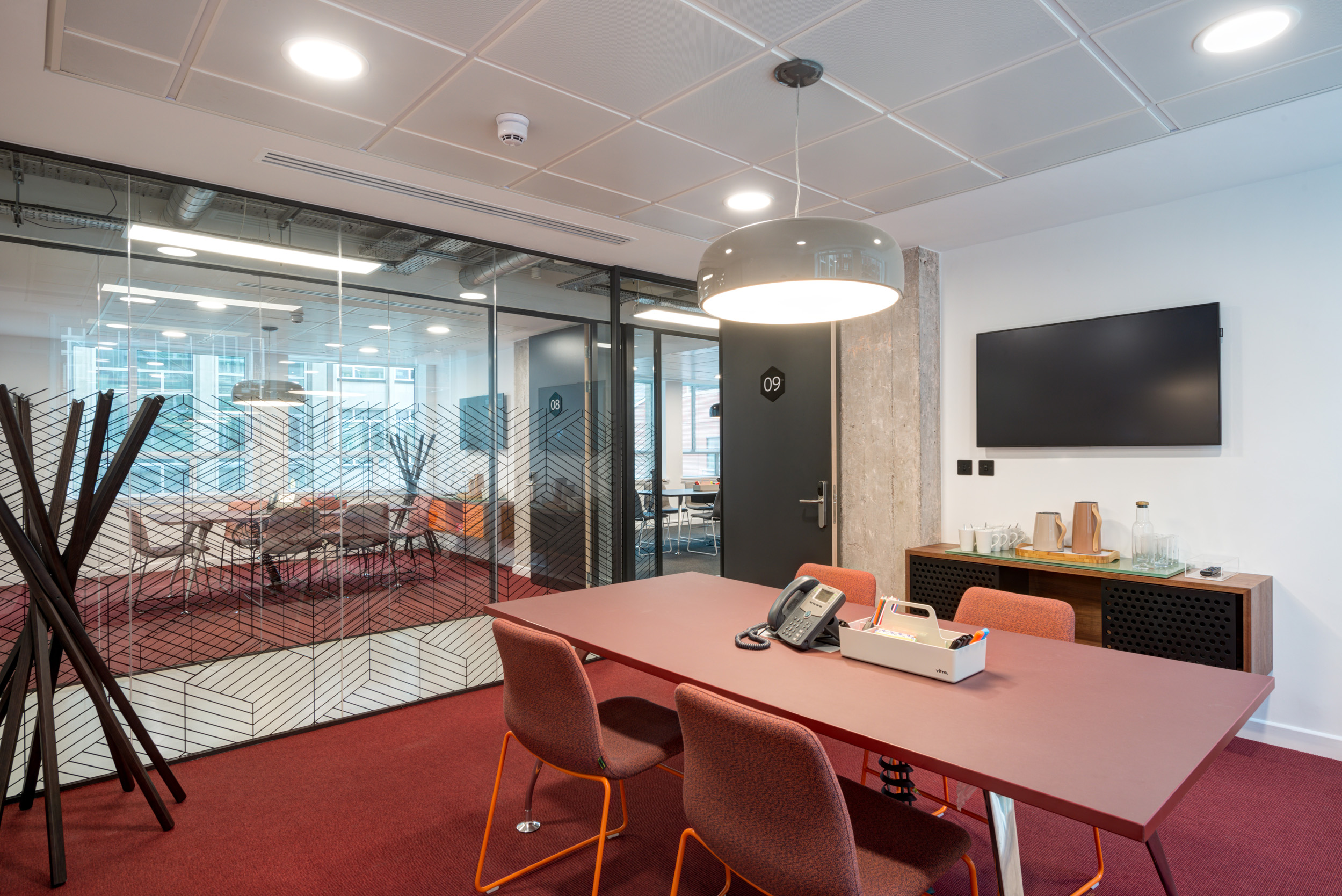A conference room with a red table, pink chairs, glazing, and modern lighting at Spaces Peter House, Manchester.