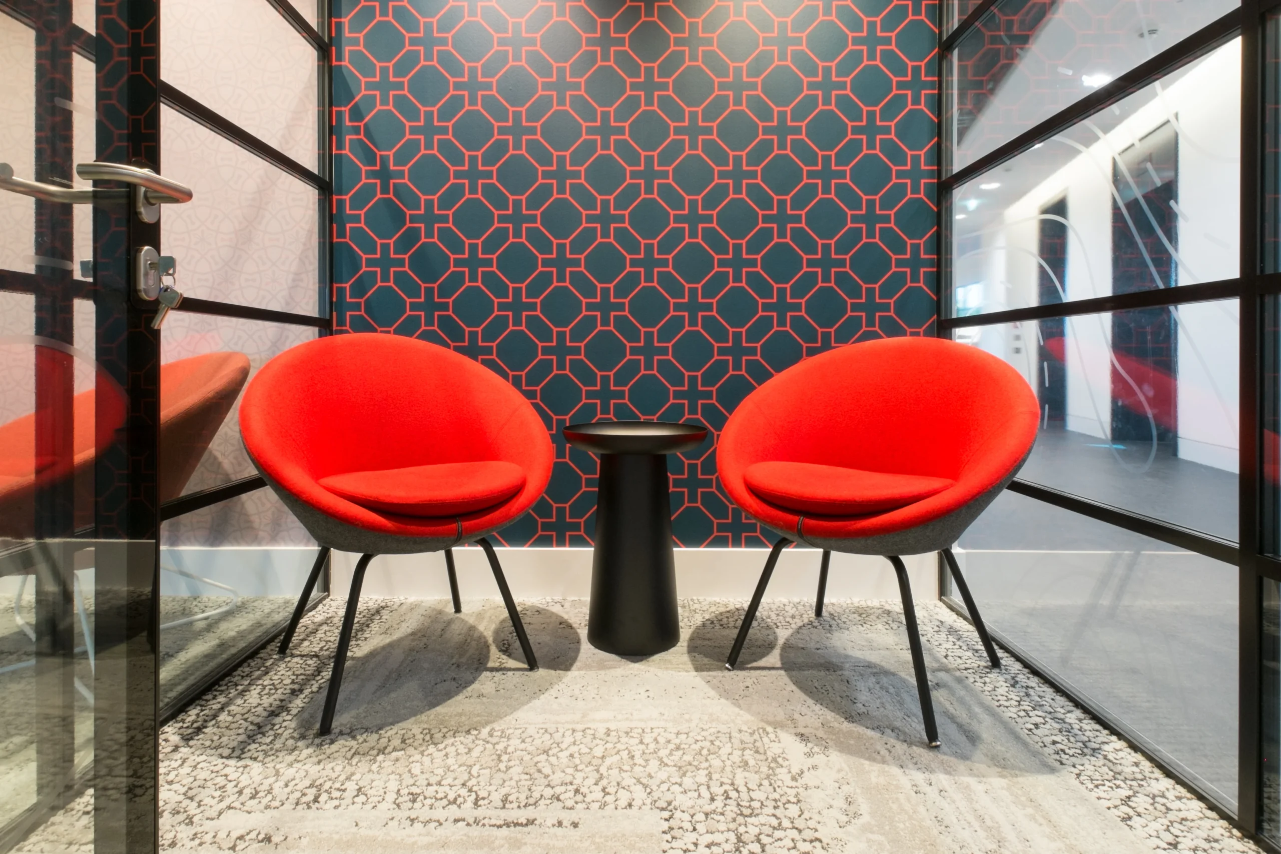 A small meeting room at Skyscanner’s office with two red chairs, a black table, and geometric wall patterns.