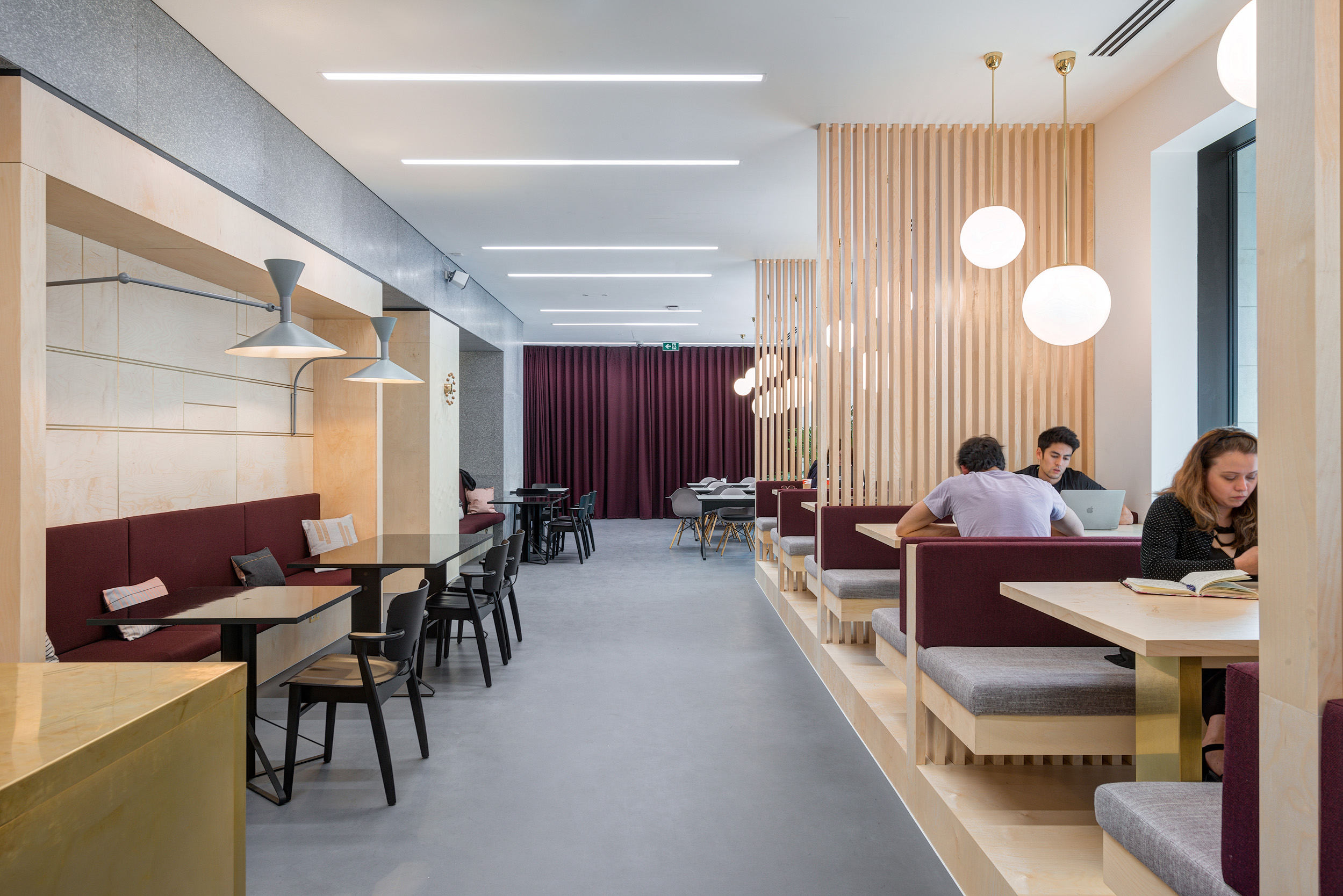 Bright and spacious communal seating with light wood dividers and maroon upholstered booths at Spaces Harley Building.