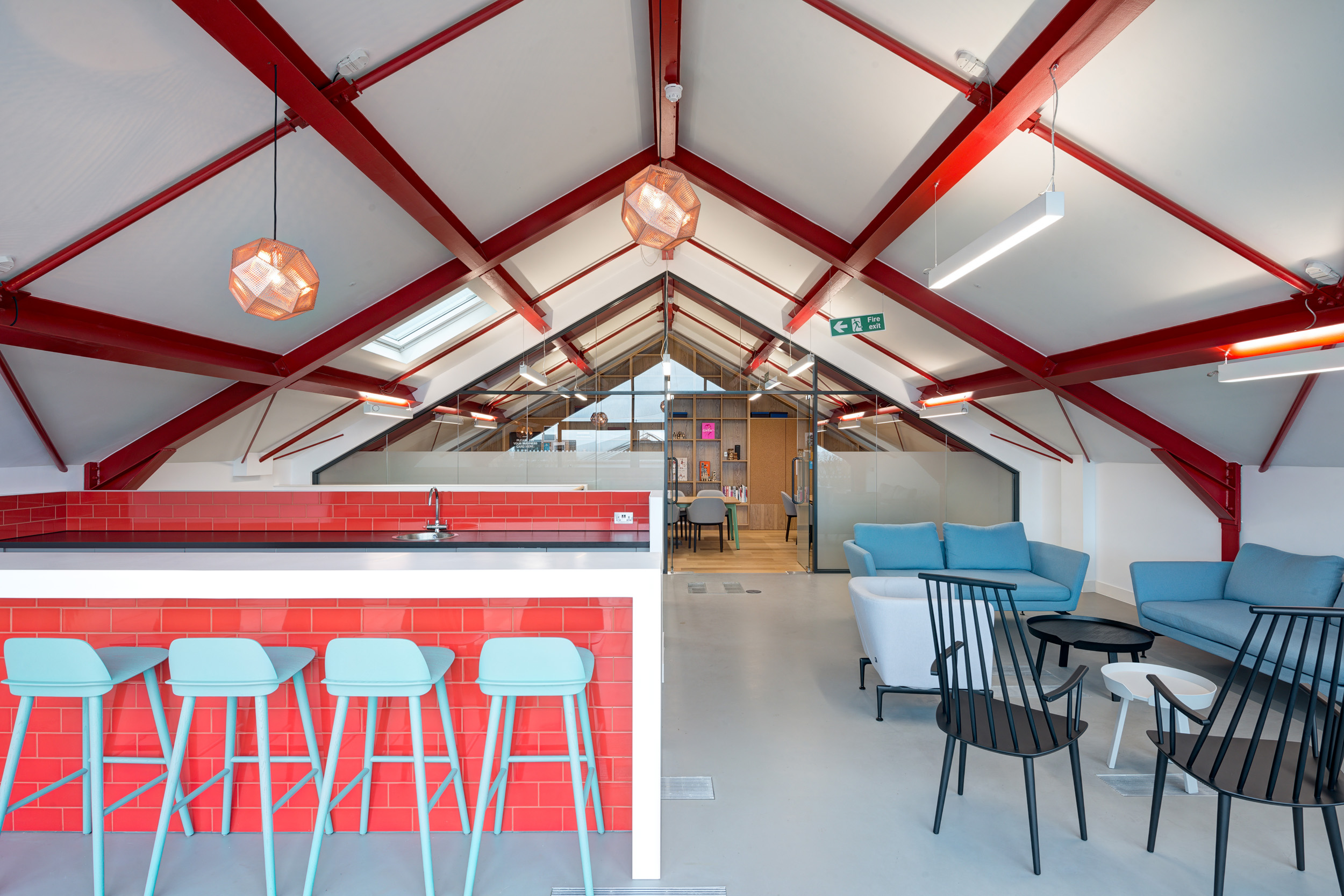 A breakout area in Spaces Mocatta House's loft space in Brighton features bold red beams, contemporary seating, and a teapoint.