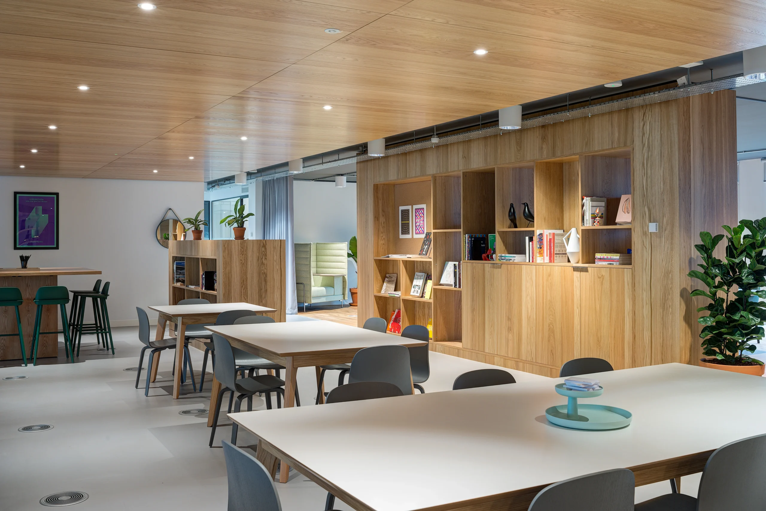 Open shelving and additional seating at Spaces Uxbridge, offering a flexible working environment with a focus on wooden accents and natural greenery.