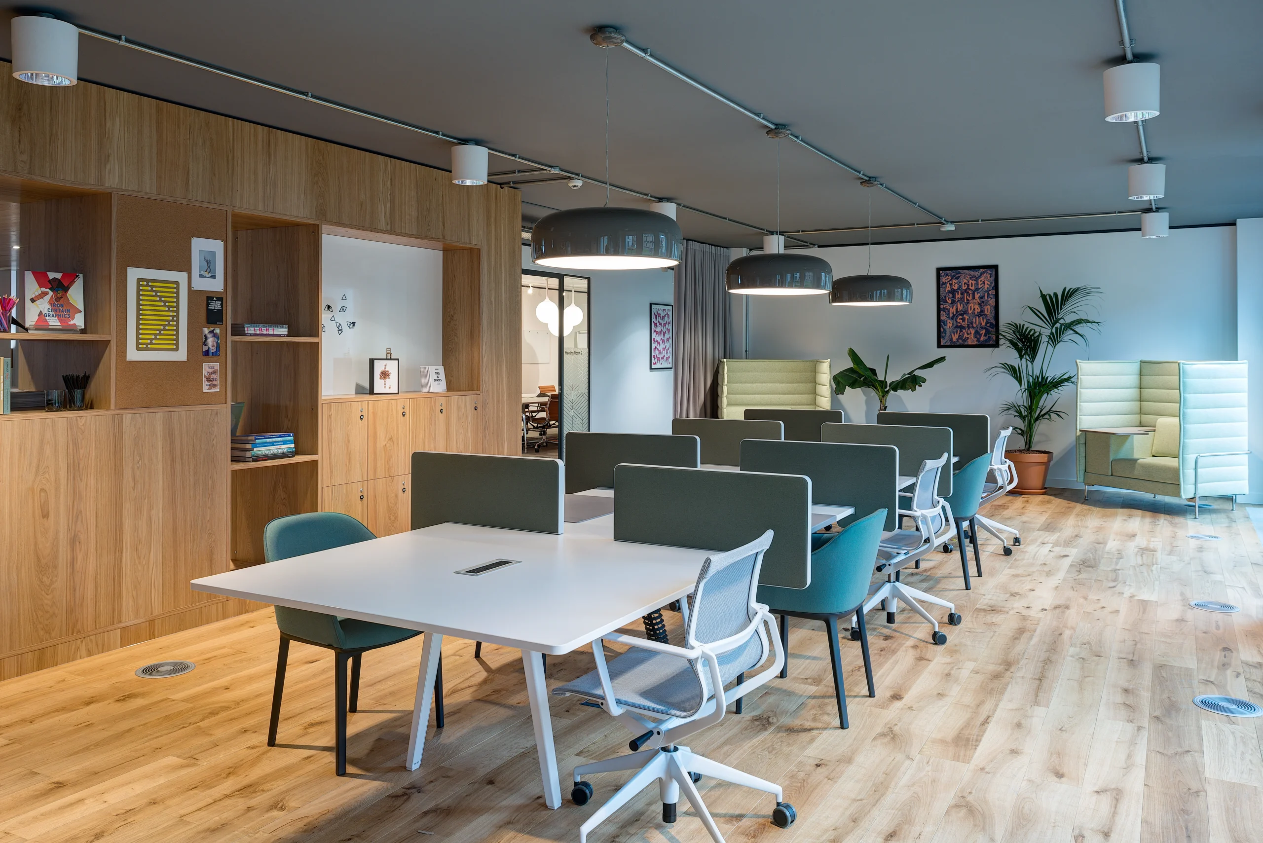 Shared desk space at Spaces Uxbridge with white desks and ergonomic chairs. Soft green chairs in the background create quiet seating zones with ample natural light.