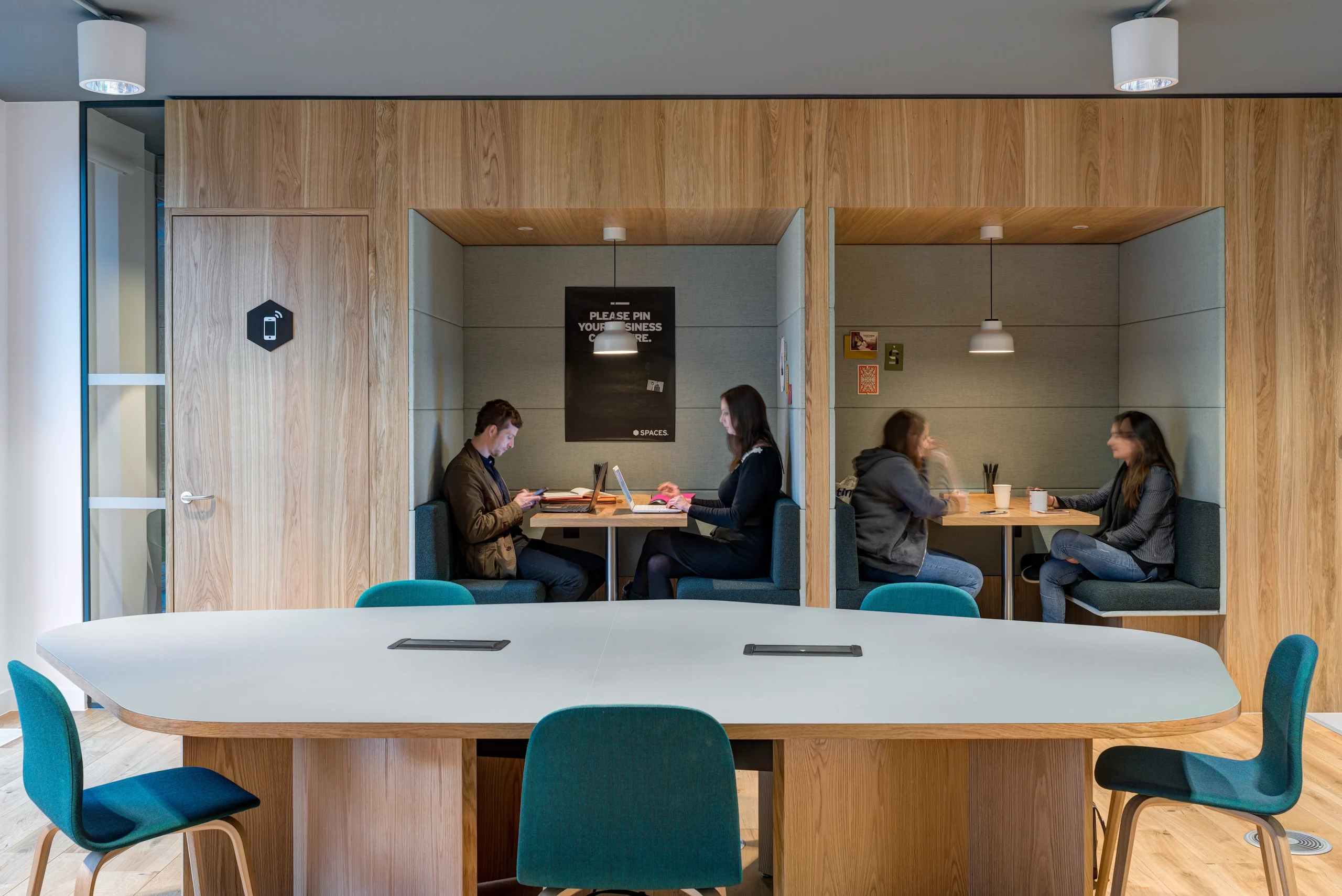 Private work booths at Spaces Uxbridge, with individuals working in a calm environment, seated at contemporary wood-lined booths for focused tasks.