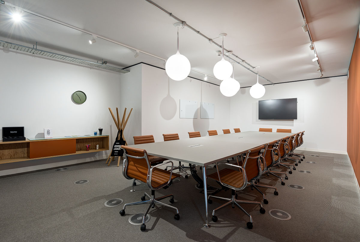 A boardroom at Spaces Uxbridge with a long table, brown leather office chairs, and bright globe lighting.