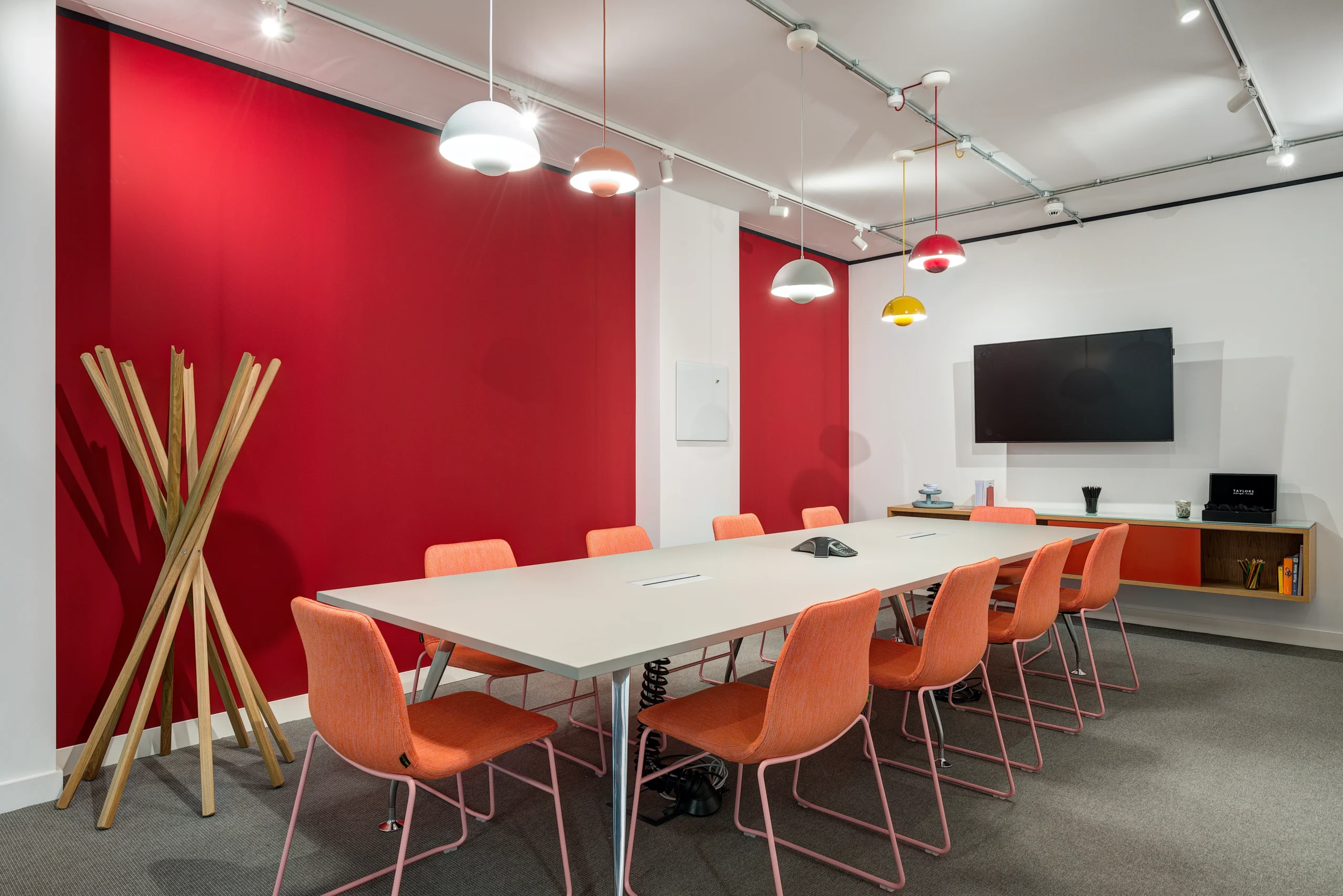 A vibrant meeting room at Spaces Uxbridge with bold red walls, colourful pendant lighting, and orange chairs.