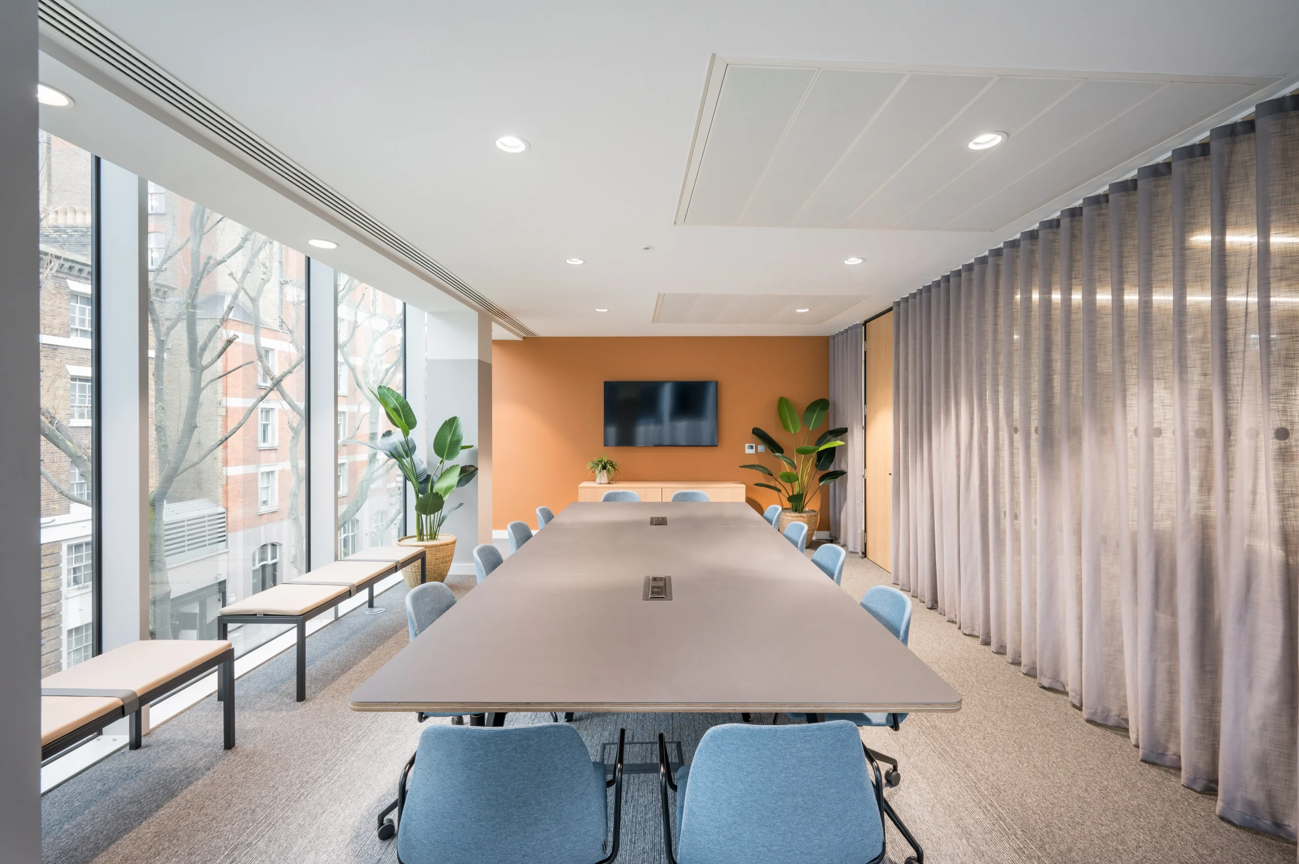 A sleek, large meeting room with a long table surrounded by blue chairs. The room is bordered with large windows, providing ample natural light and views of urban surroundings, part of Modus’s design for State Street Global Advisors.