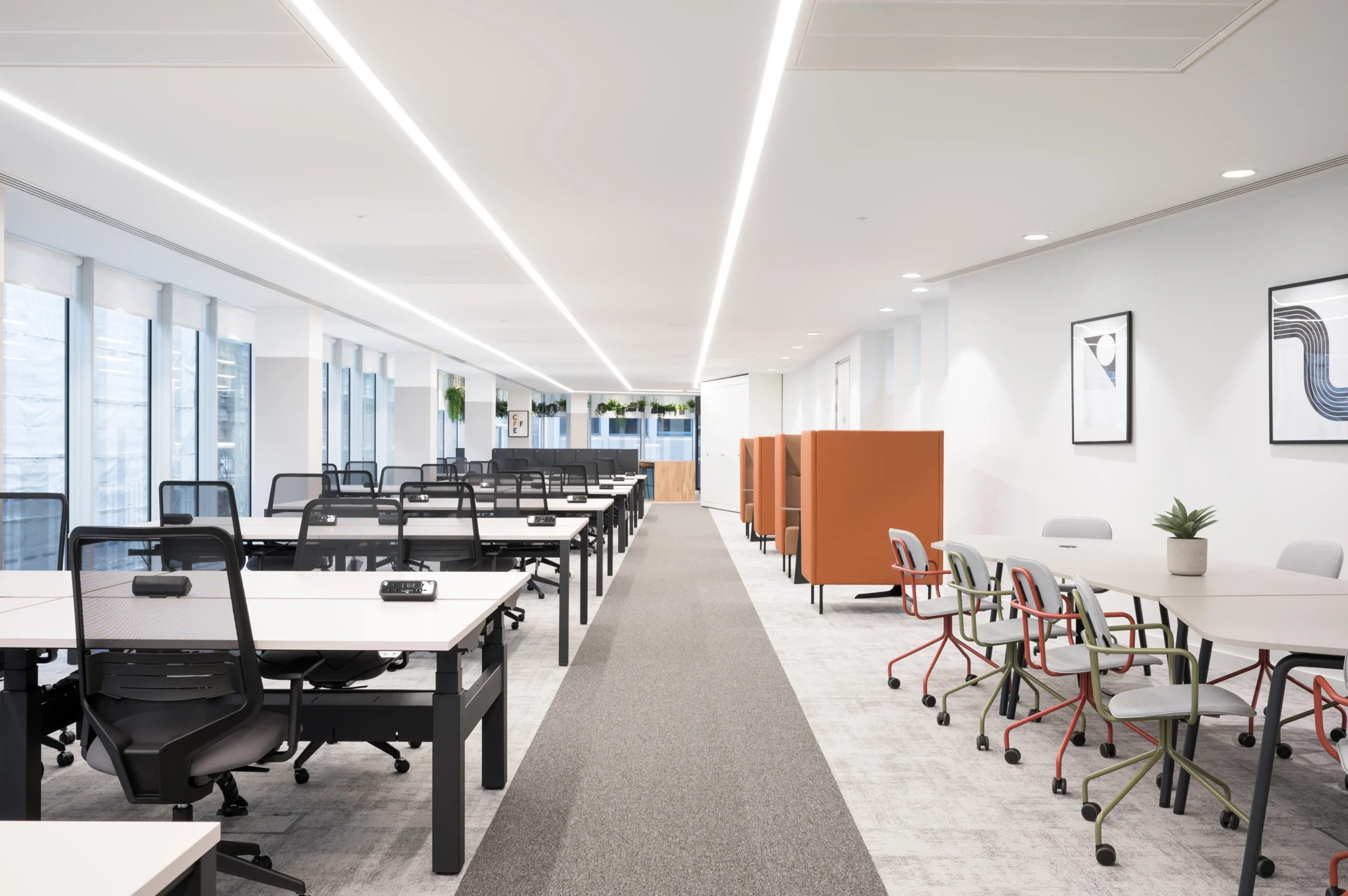 Long view of a spacious modern office with rows of black and white desks and orange privacy panels. The room is well-lit with sleek, linear lighting and features hanging green plants and minimalist wall art. Designed by Modus for State Street Global Advisors.