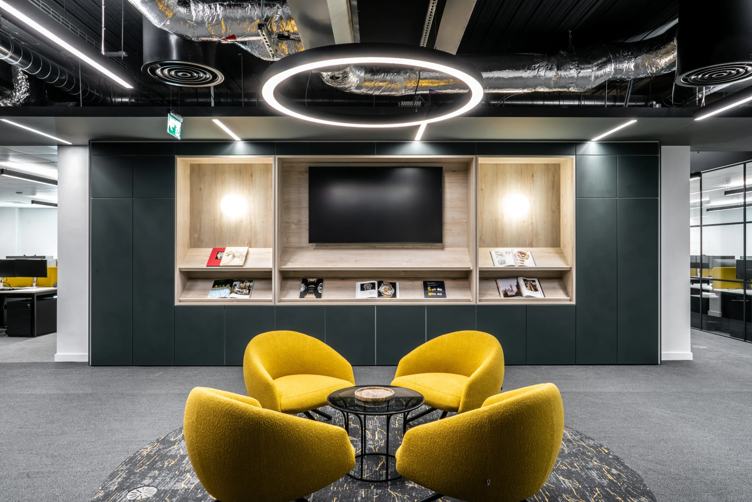The Watches of Switzerland Group open -plan seating area with vibrant yellow seats, bespoke hanging lighting, a large screen, and books decorating the space.