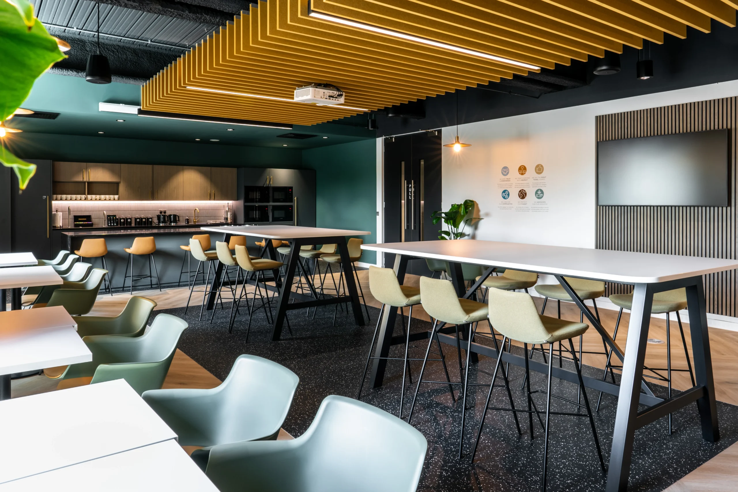 The Watches of Switzerland Group bespoke teapoint, with tall chairs, branded coloured acoustic panelling and plants.