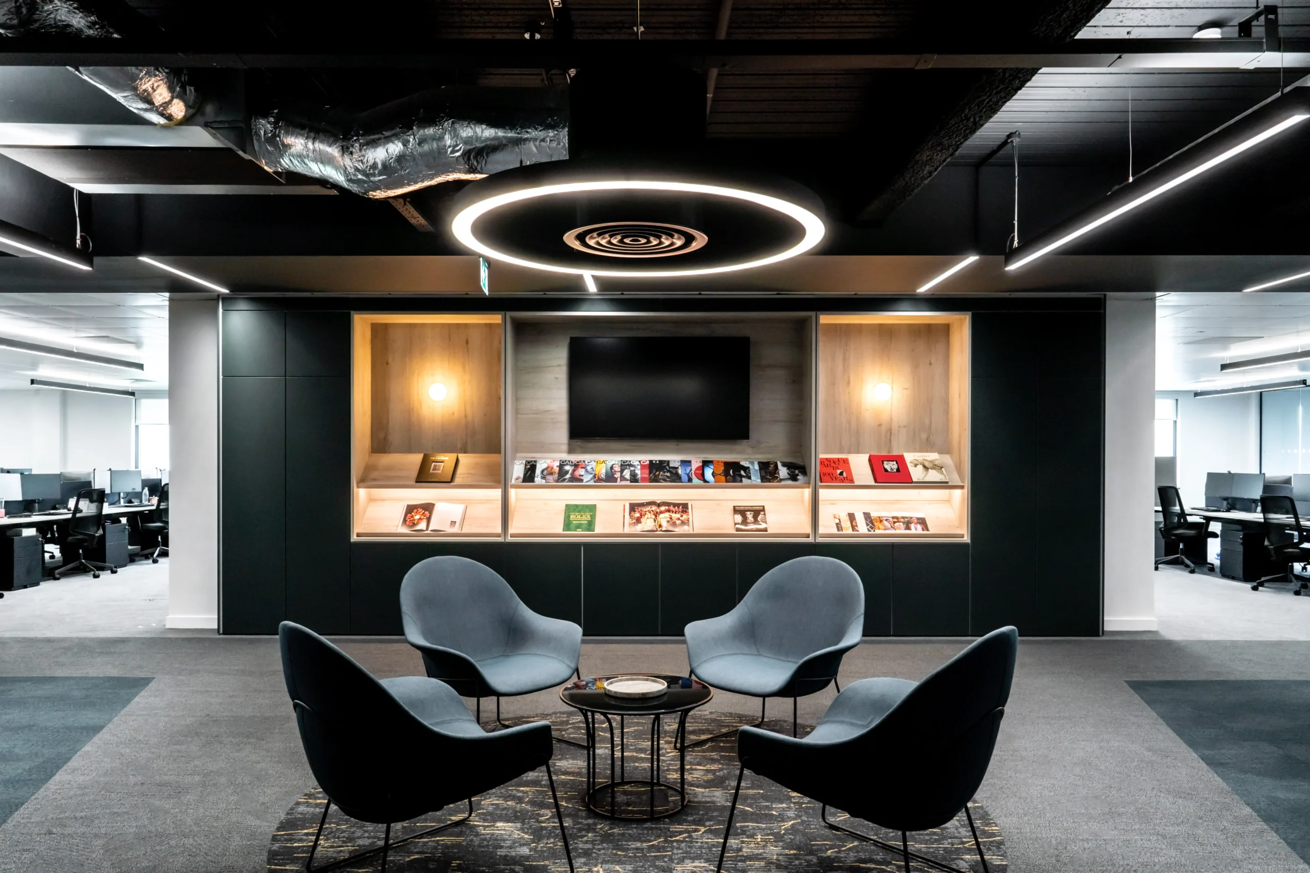 Stylish open - plan workspace with grey seating, bespoke hanging lights, and exposed ceiling.