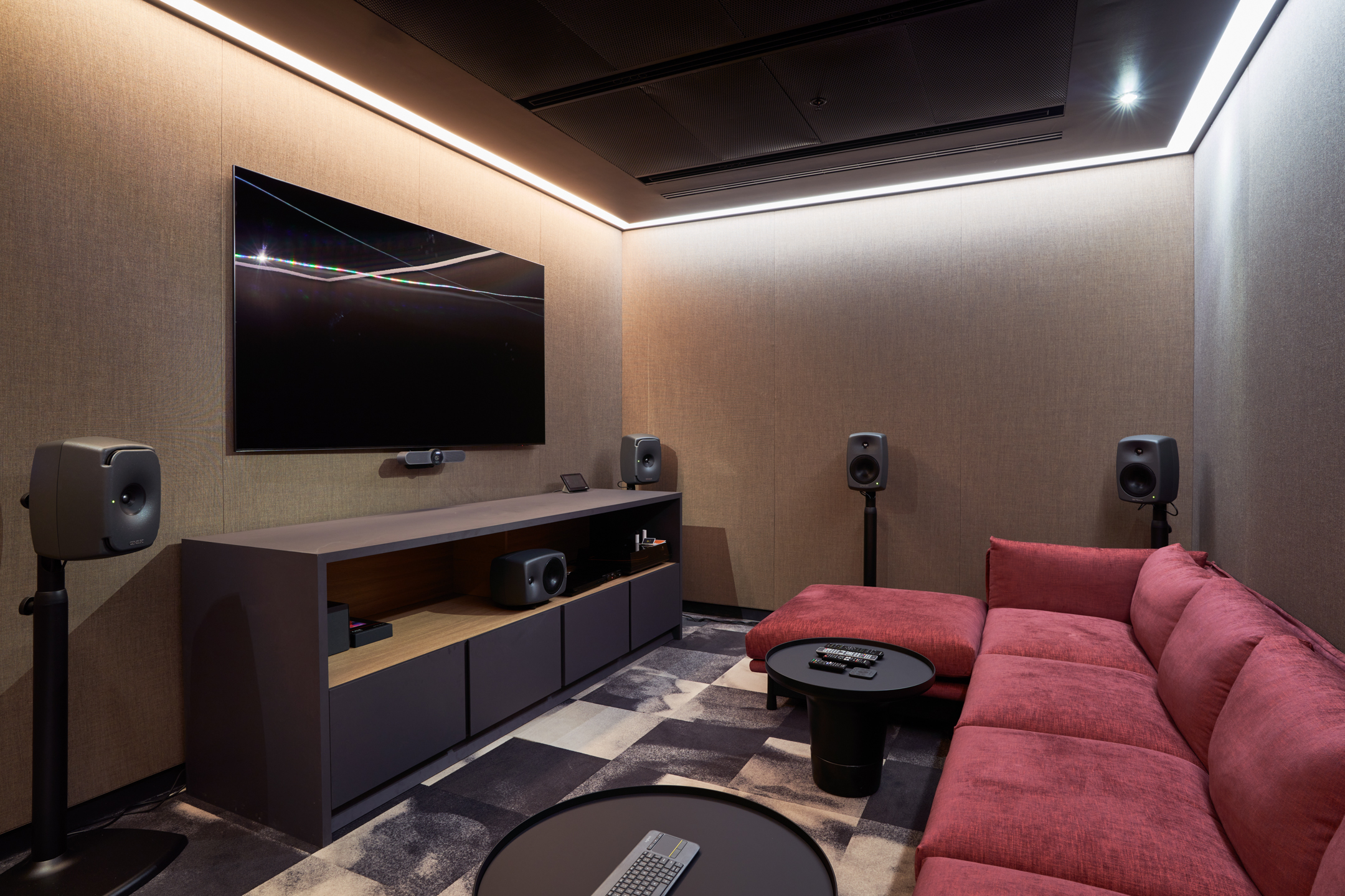 Luxury Media Viewing Room: This sophisticated viewing room at United Talent Agency features a large, plush red sofa, state-of-the-art speakers, and a wall-mounted TV. The design by Modus includes textured beige wall coverings and accent lighting that creates a warm, inviting space for viewing and presentations.