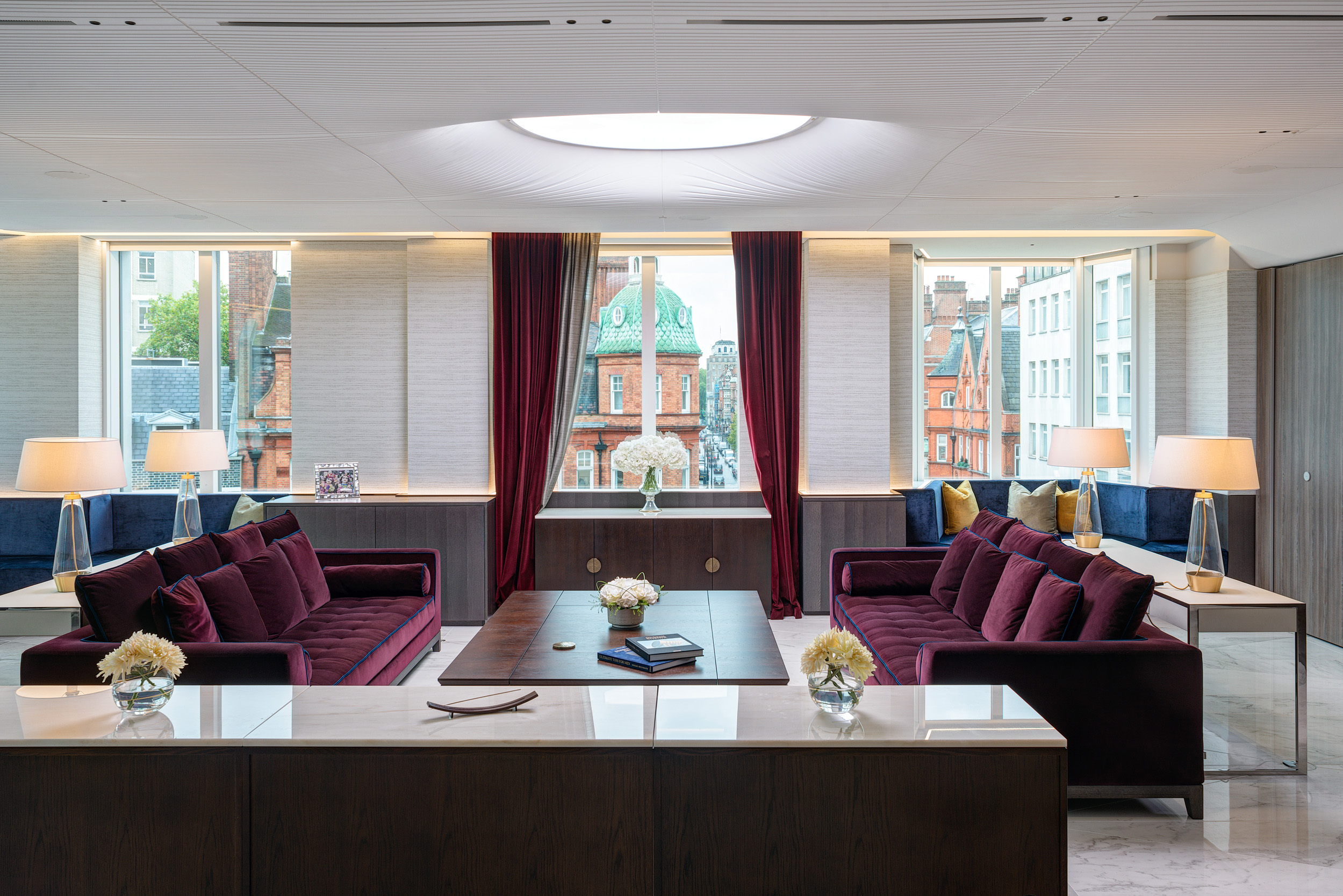 Vedanta's executive lounge offers rich burgundy sofas and deep blue window seating, framed by large windows with views of historic architecture. Designed by Modus Workspace, this luxurious yet serene space is ideal for discussions.