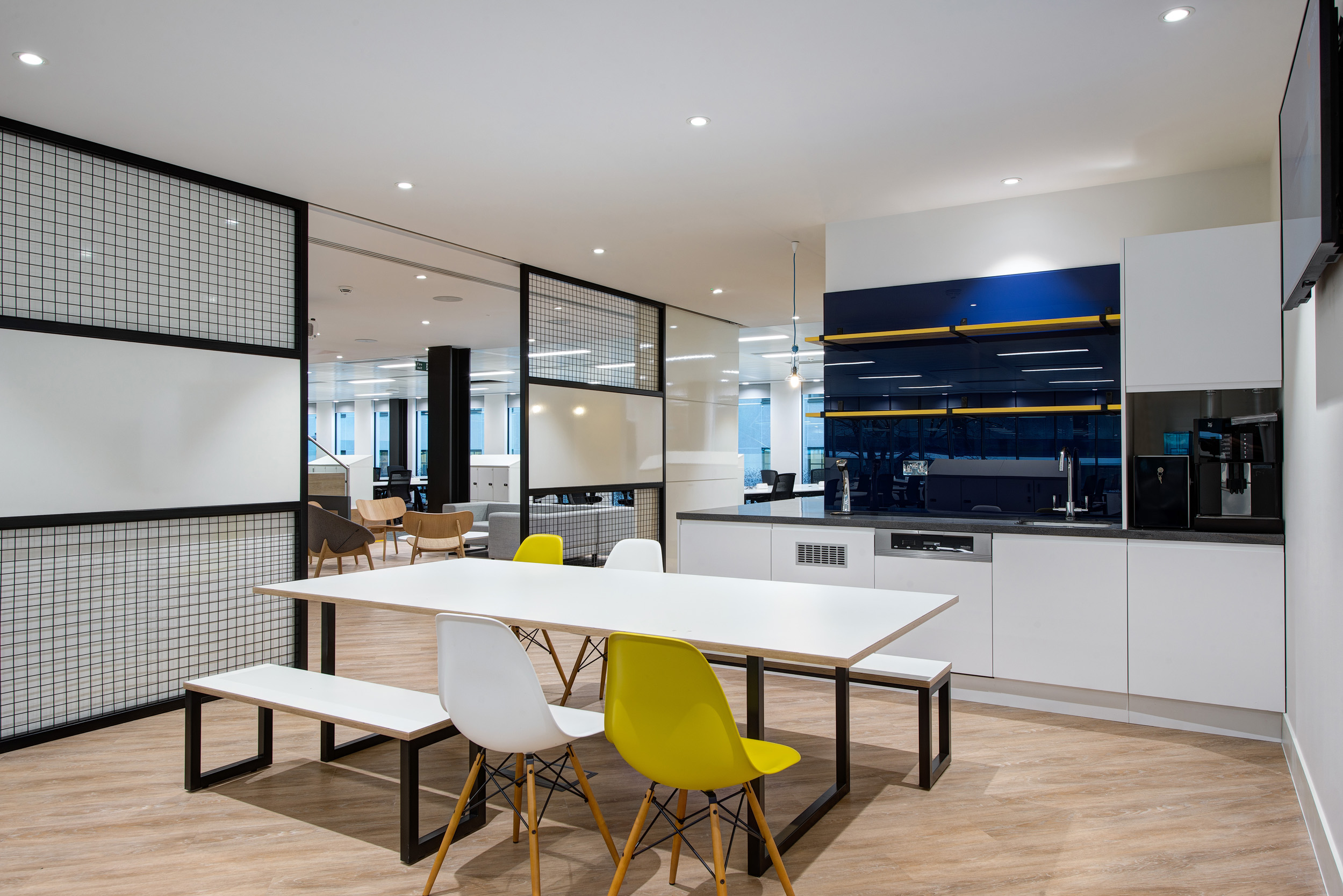 The teapoint and dining space at William Hill provides a modern, functional area with ample seating, bright lighting, and sleek design finishes, designed by Modus Workspace.
