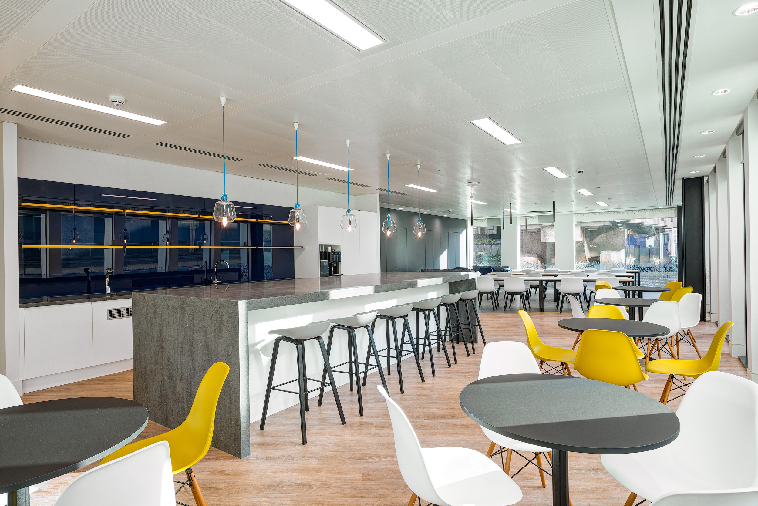 A contemporary dining area at William Hill, designed by Modus Workspace, with colourful seating, modern pendant lighting, and large tables, perfect for employee gatherings and meals.