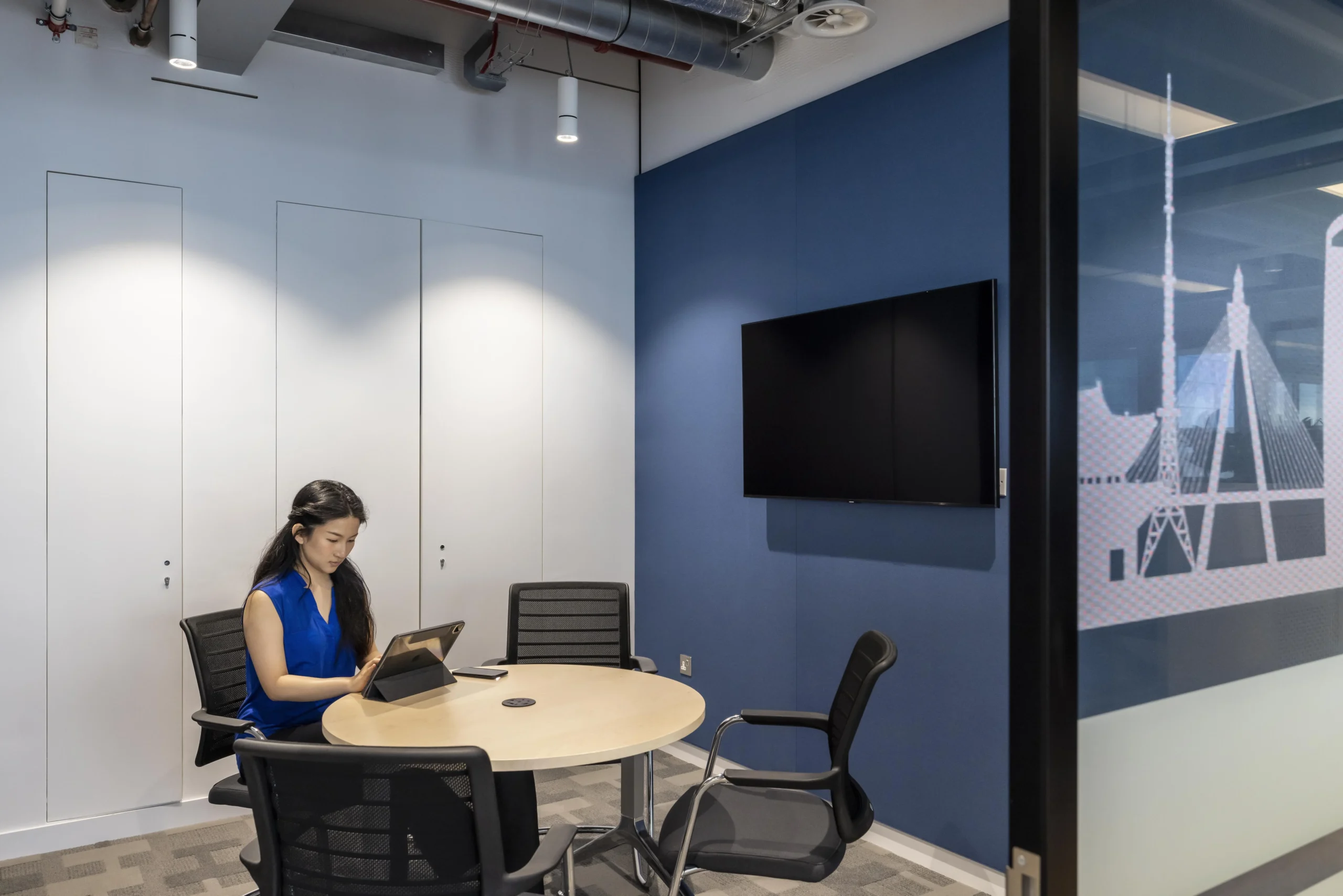 Investment Company private meeting room with a screen, branded blue walls and a frosted glass partition doors.